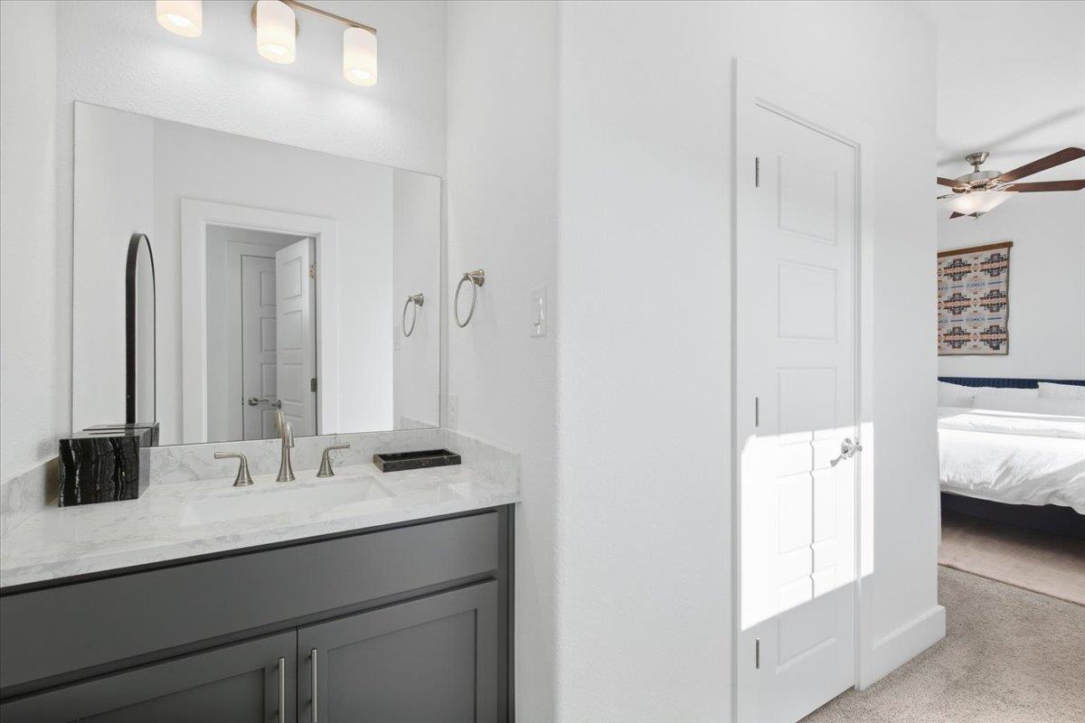 Bathroom vanity with a marble-look counter and large mirror, with a bedroom visible through the doorway.
