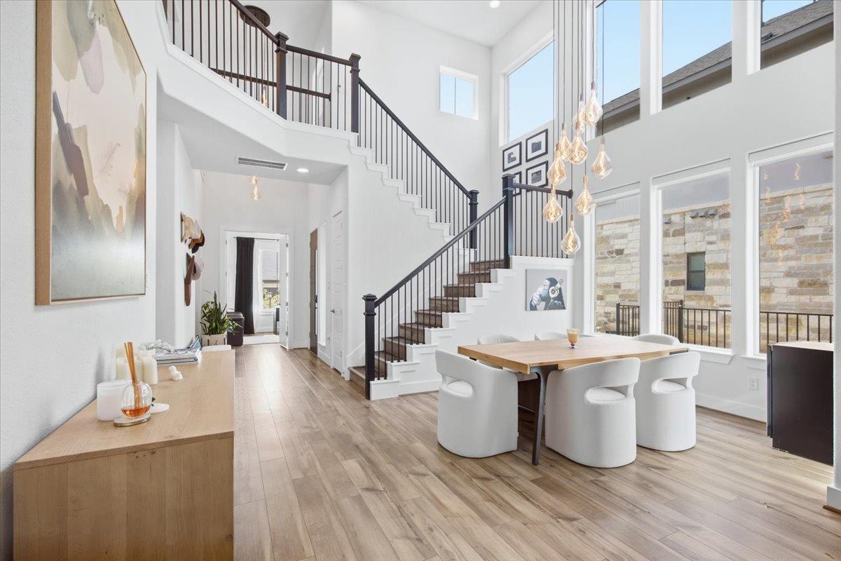 Open dining area with a tall staircase, dark railings, and large windows.
