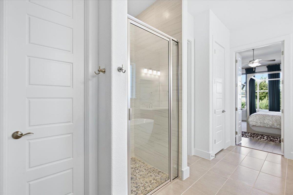 Bright bathroom with a glass shower enclosure and pebble floor, opening toward a bedroom.