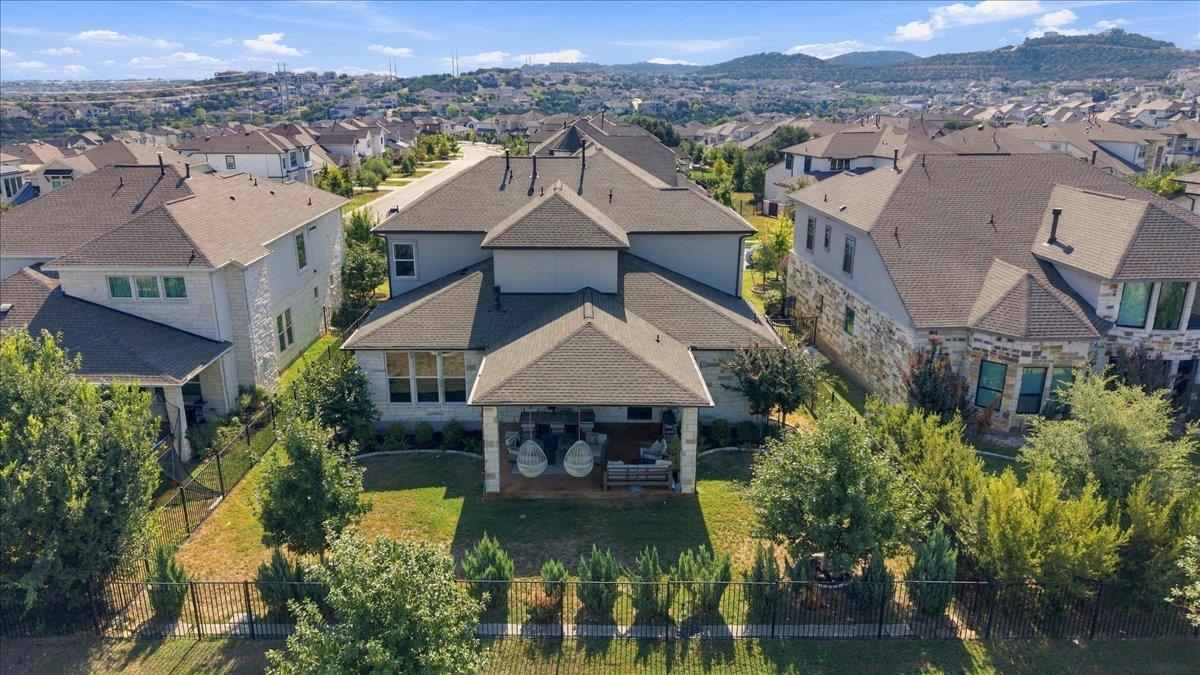 Aerial view of a home with a covered patio and fenced backyard, surrounded by houses and distant hills.
