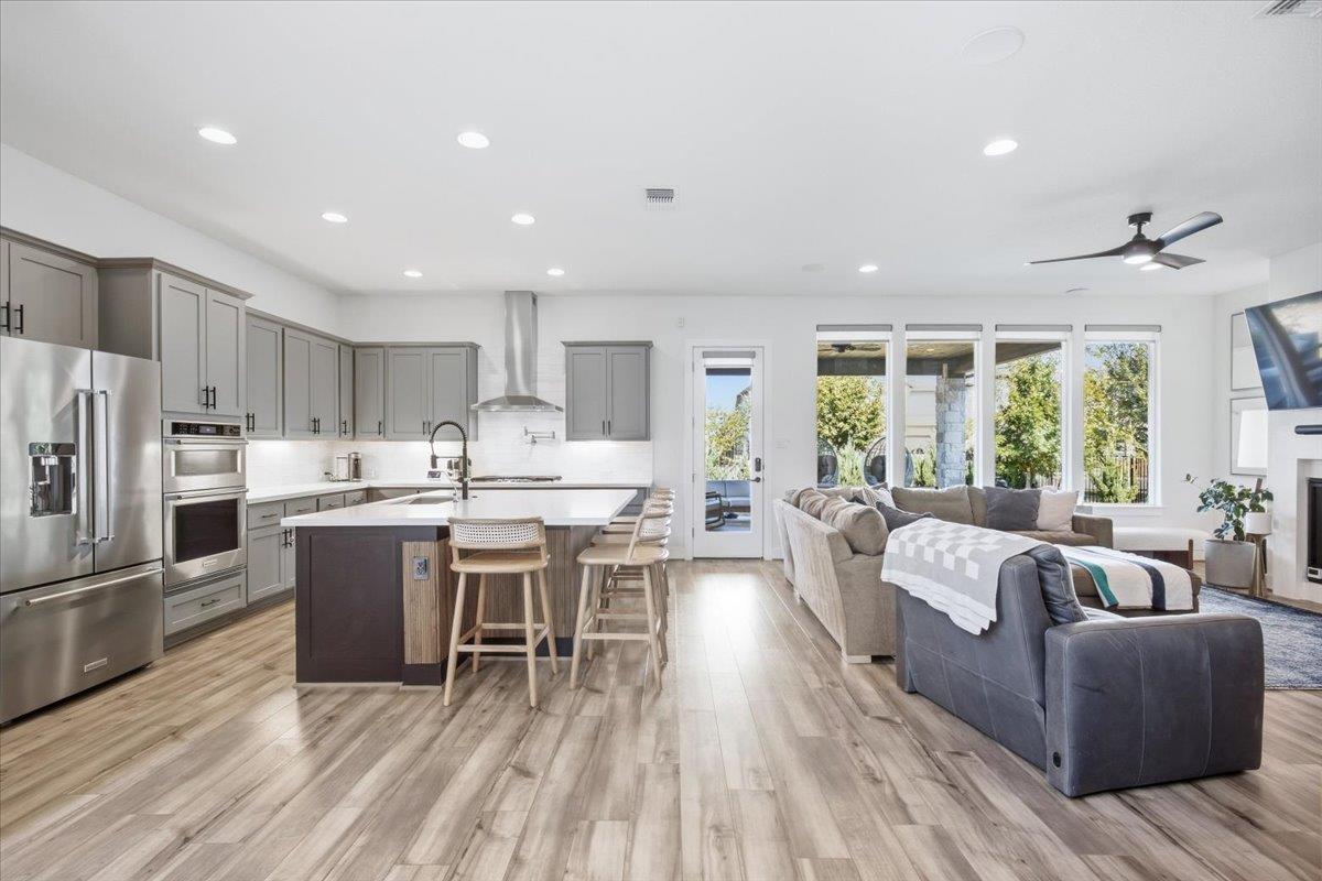 Open-plan kitchen and living room with a gray-cabinet kitchen island and a sectional sofa by wide windows.
