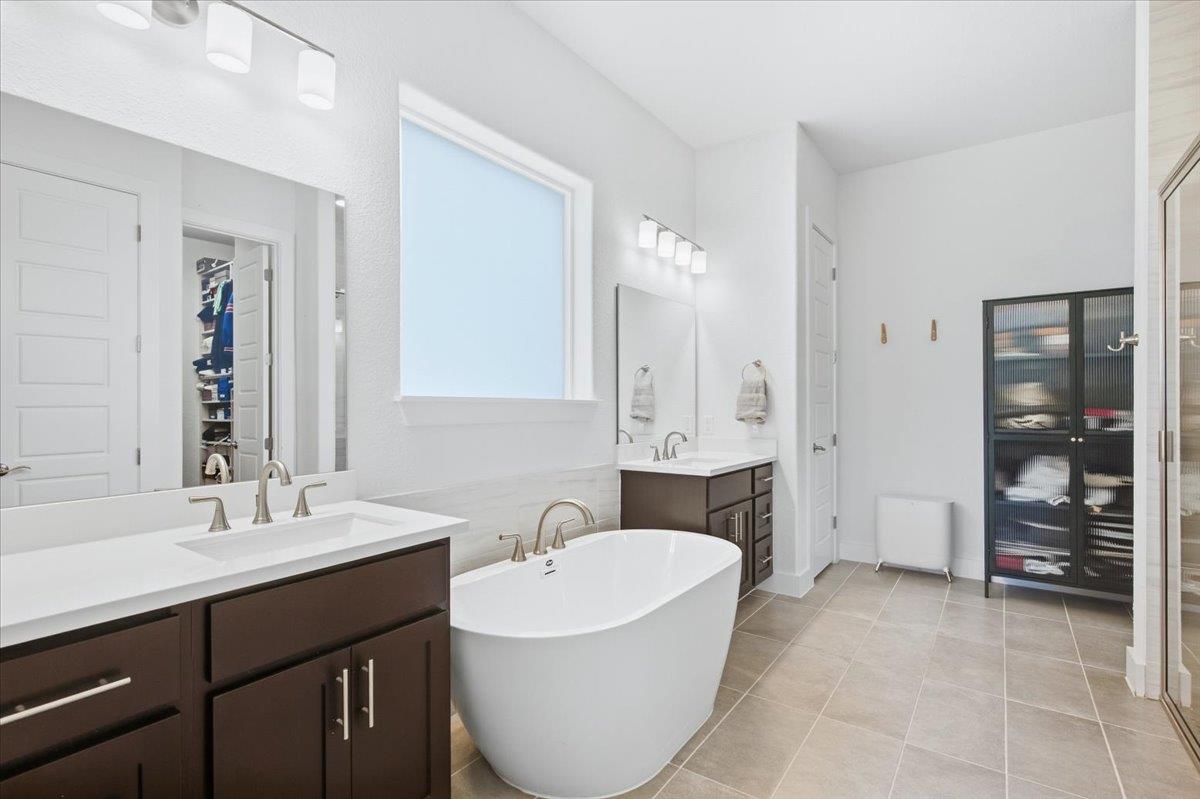 Bathroom with a freestanding soaking tub, dark double vanity, and glass-front storage cabinet.