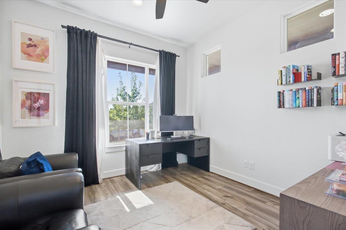 Furnished home office with a desk, floating bookshelves, and a large curtained window.