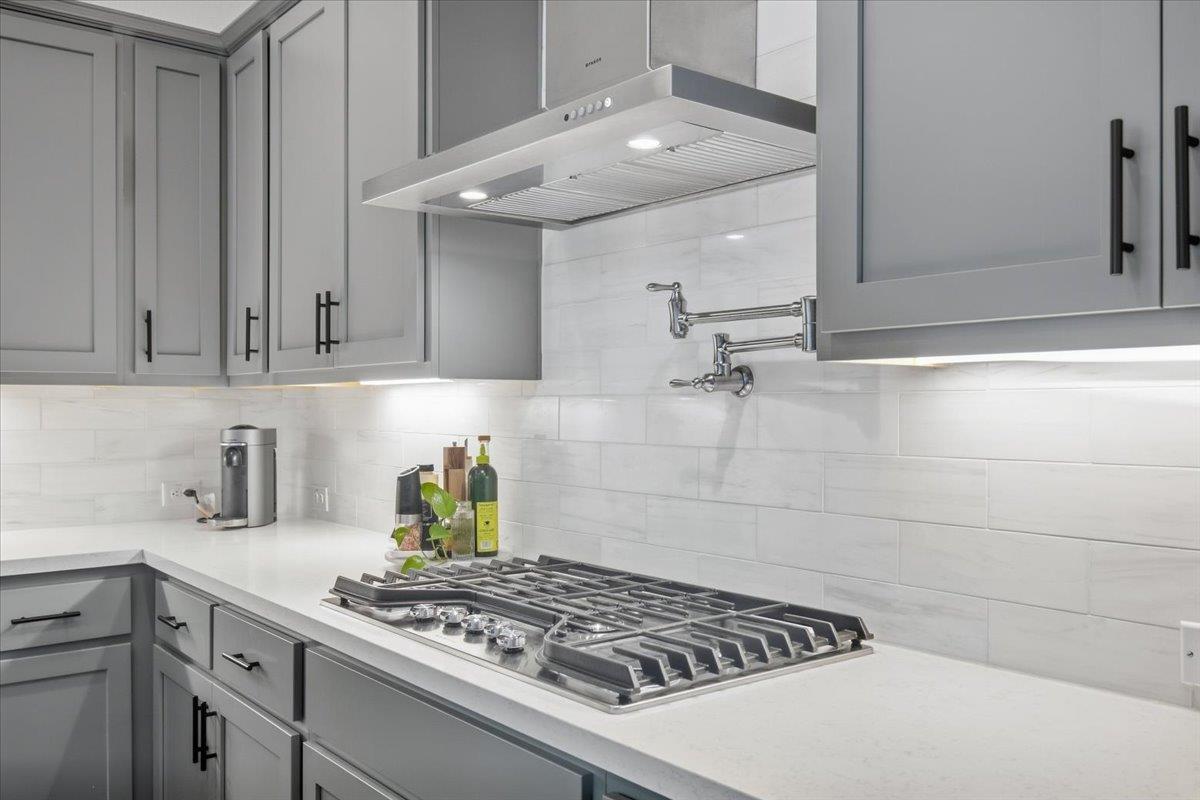 Modern kitchen with gray cabinets, a gas cooktop, and a wall-mounted pot filler.