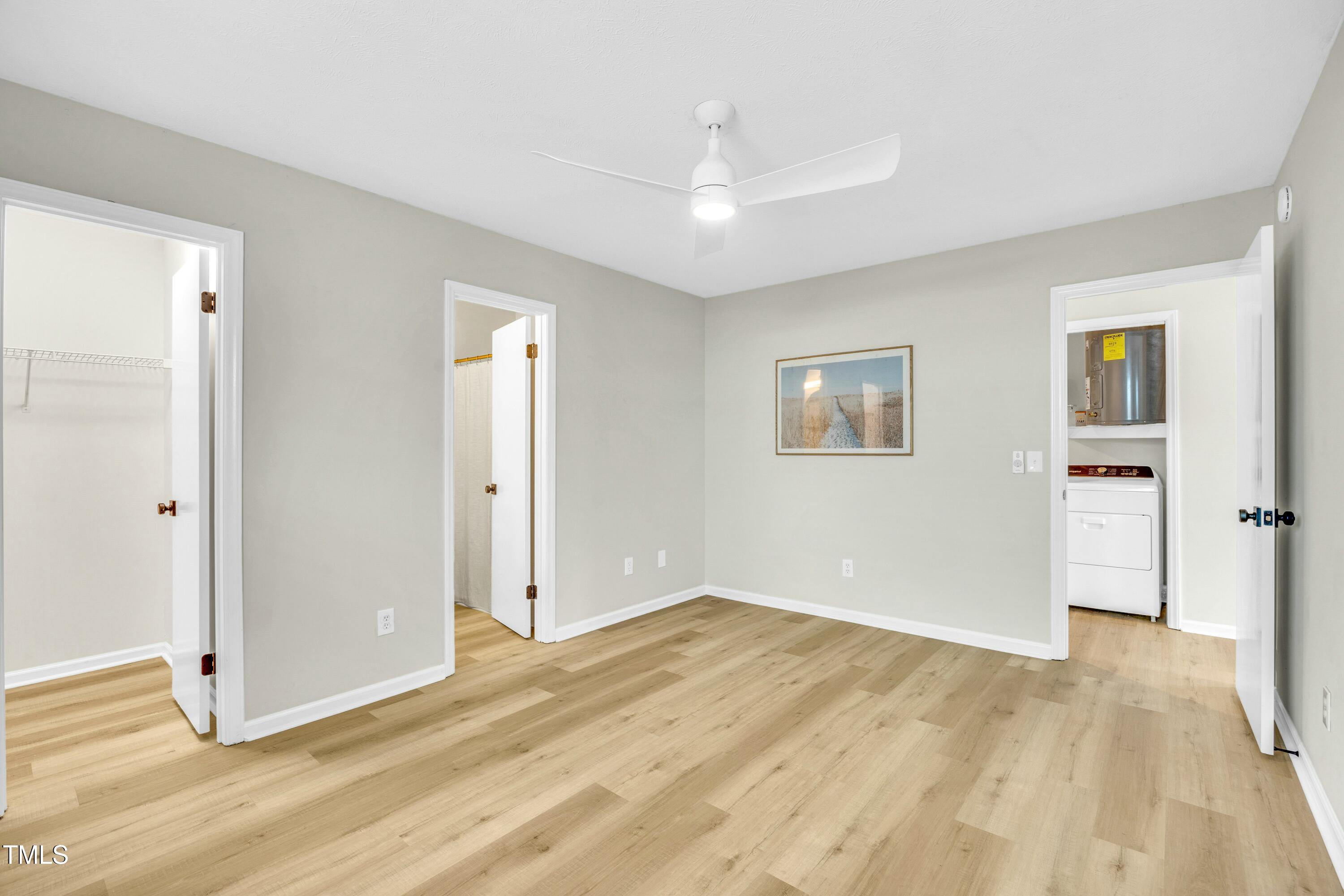 Unfurnished bedroom with light wood flooring, a ceiling fan, and doors to closets and laundry.