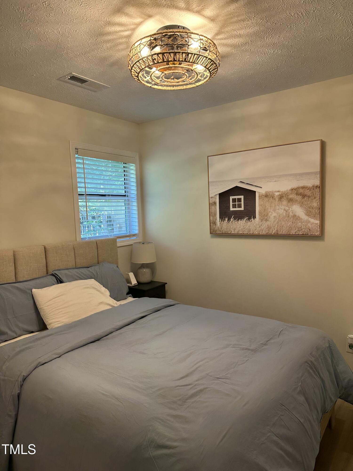 Bedroom with gray bedding, a beige headboard, and framed coastal artwork.