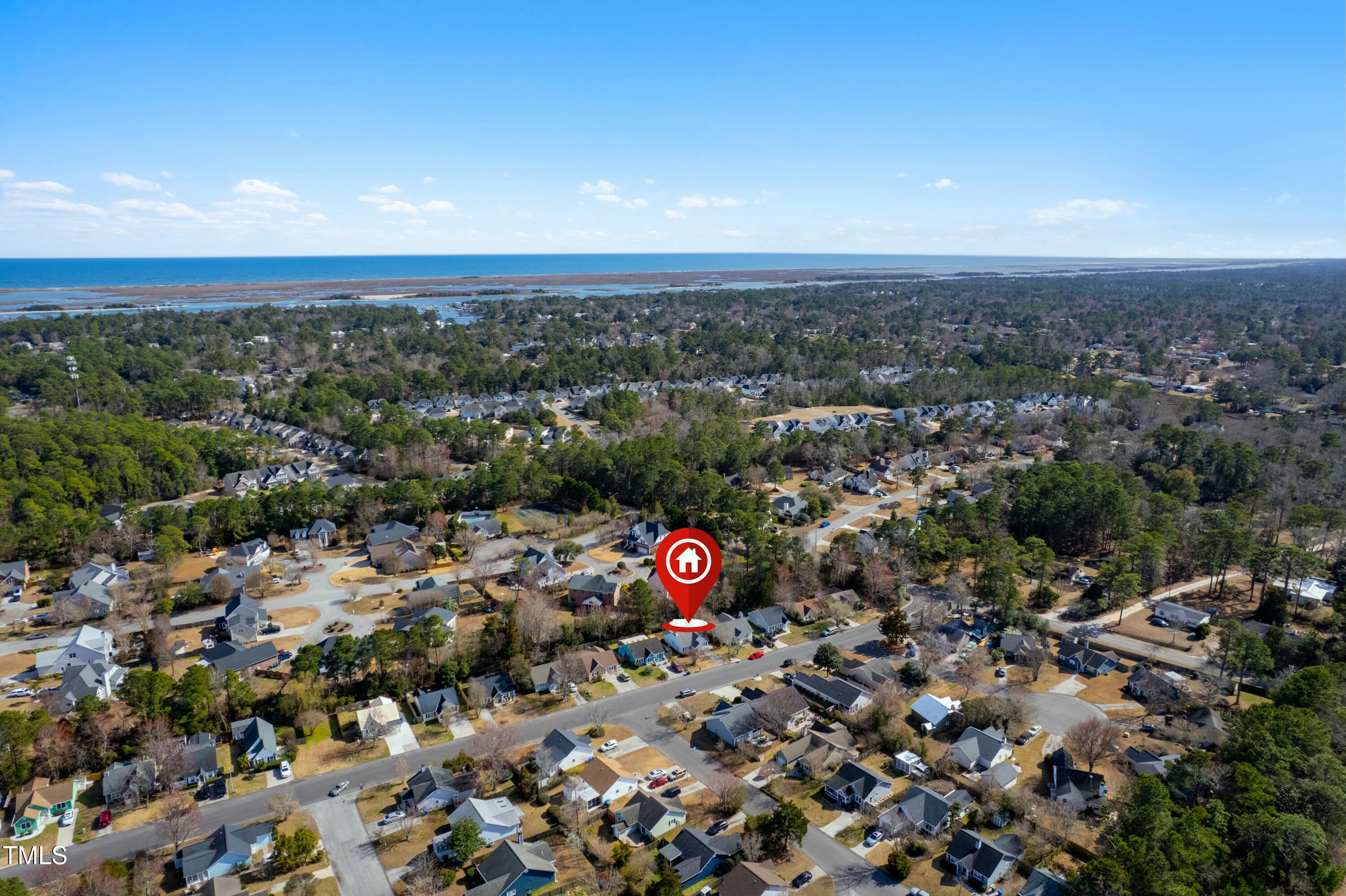 Aerial view of a wooded coastal neighborhood, with the featured home marked near the shoreline.