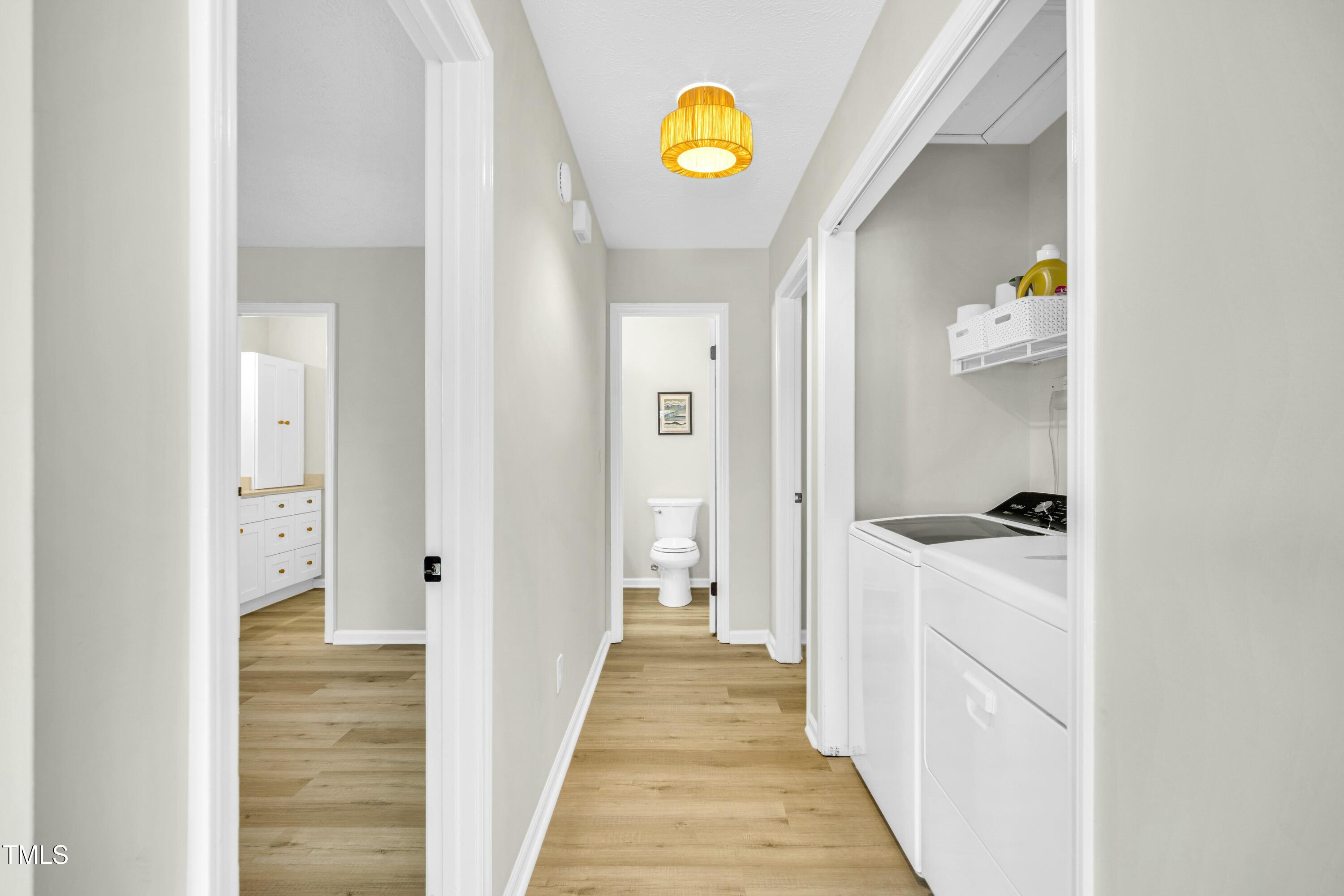 Hallway with washer and dryer, leading to a bathroom; a vanity is visible through the left doorway.