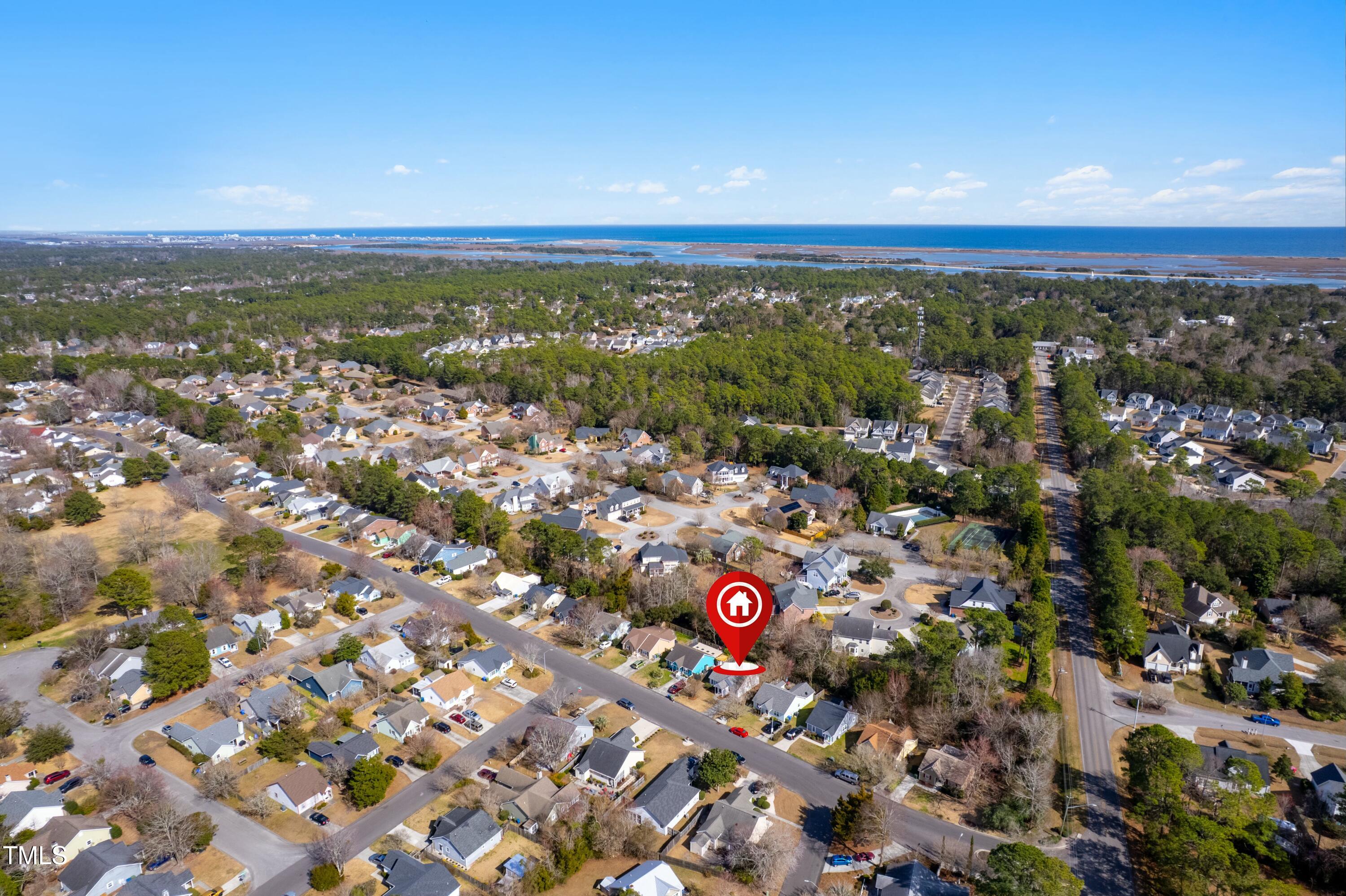 Aerial neighborhood view with a red property marker, coastal marshes, and ocean in the distance.