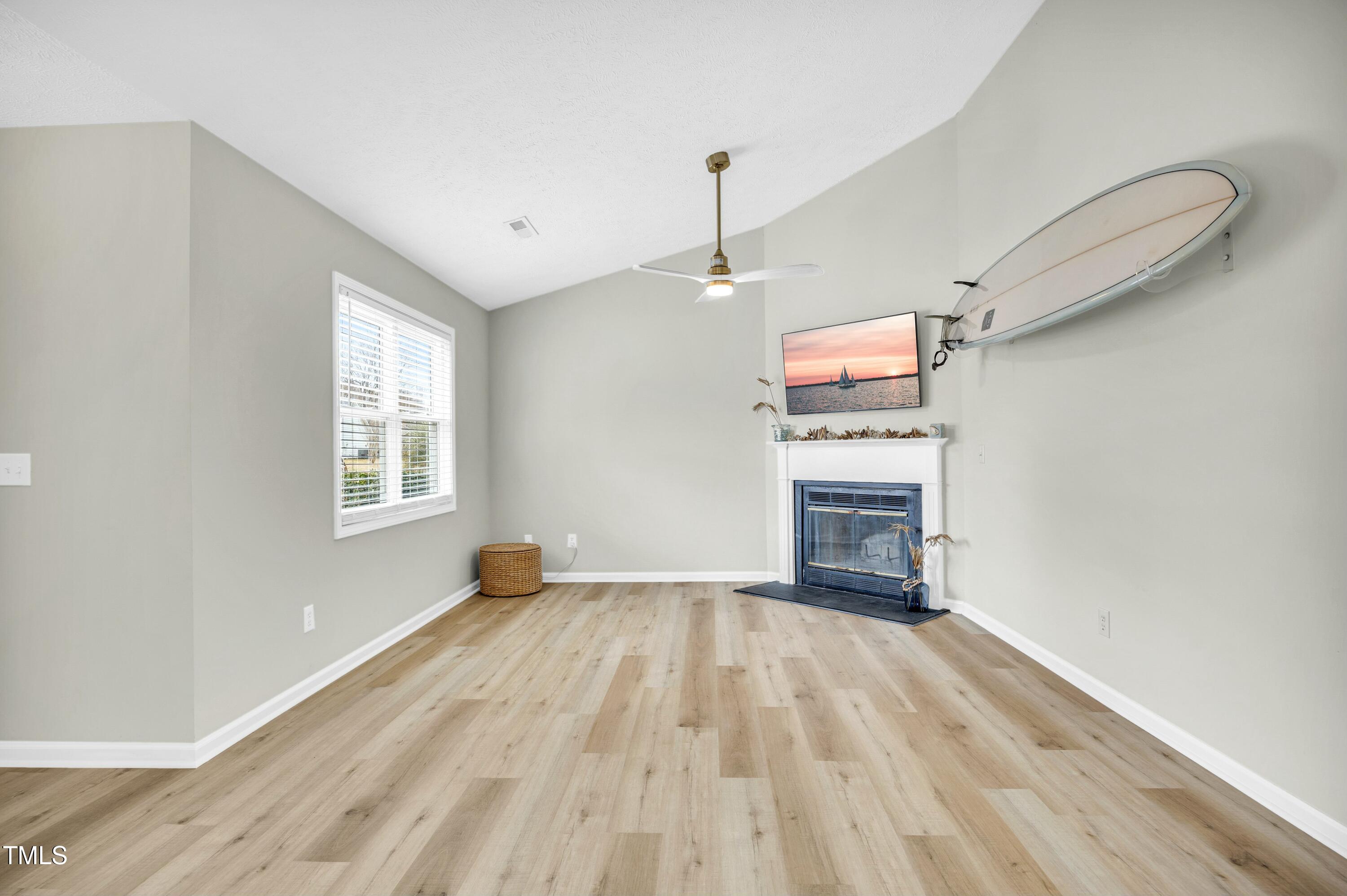 Living room with a fireplace, light wood flooring, and a wall-mounted surfboard.