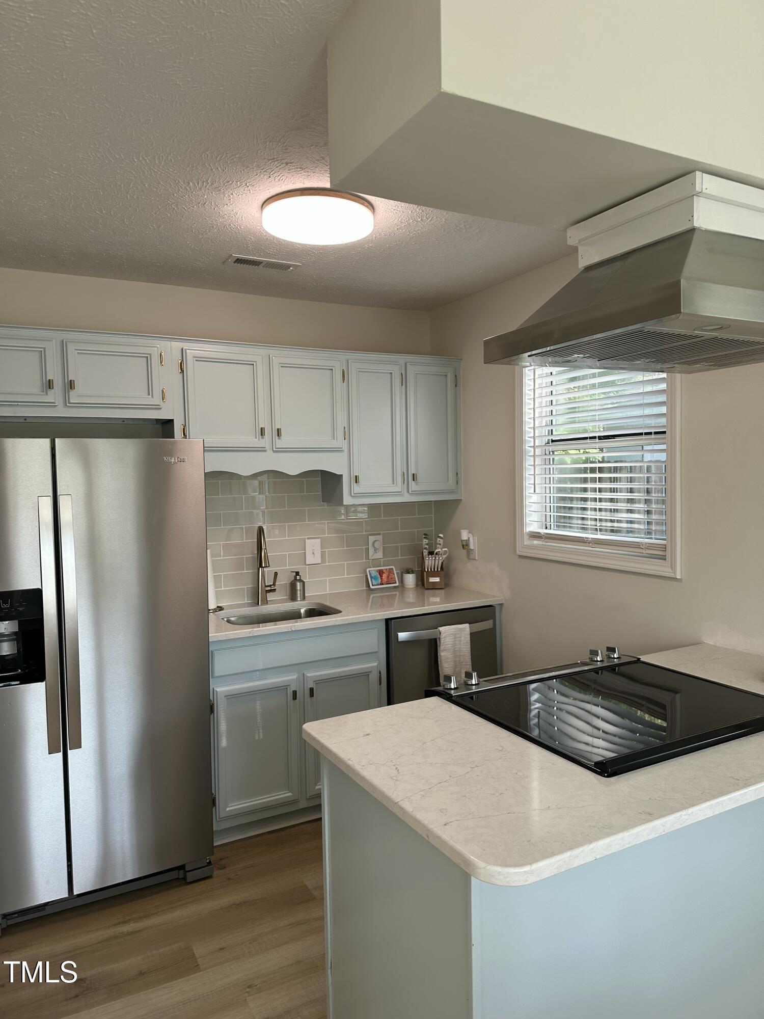 Kitchen with pale blue-gray cabinets, stainless steel appliances, and a large island with a cooktop.