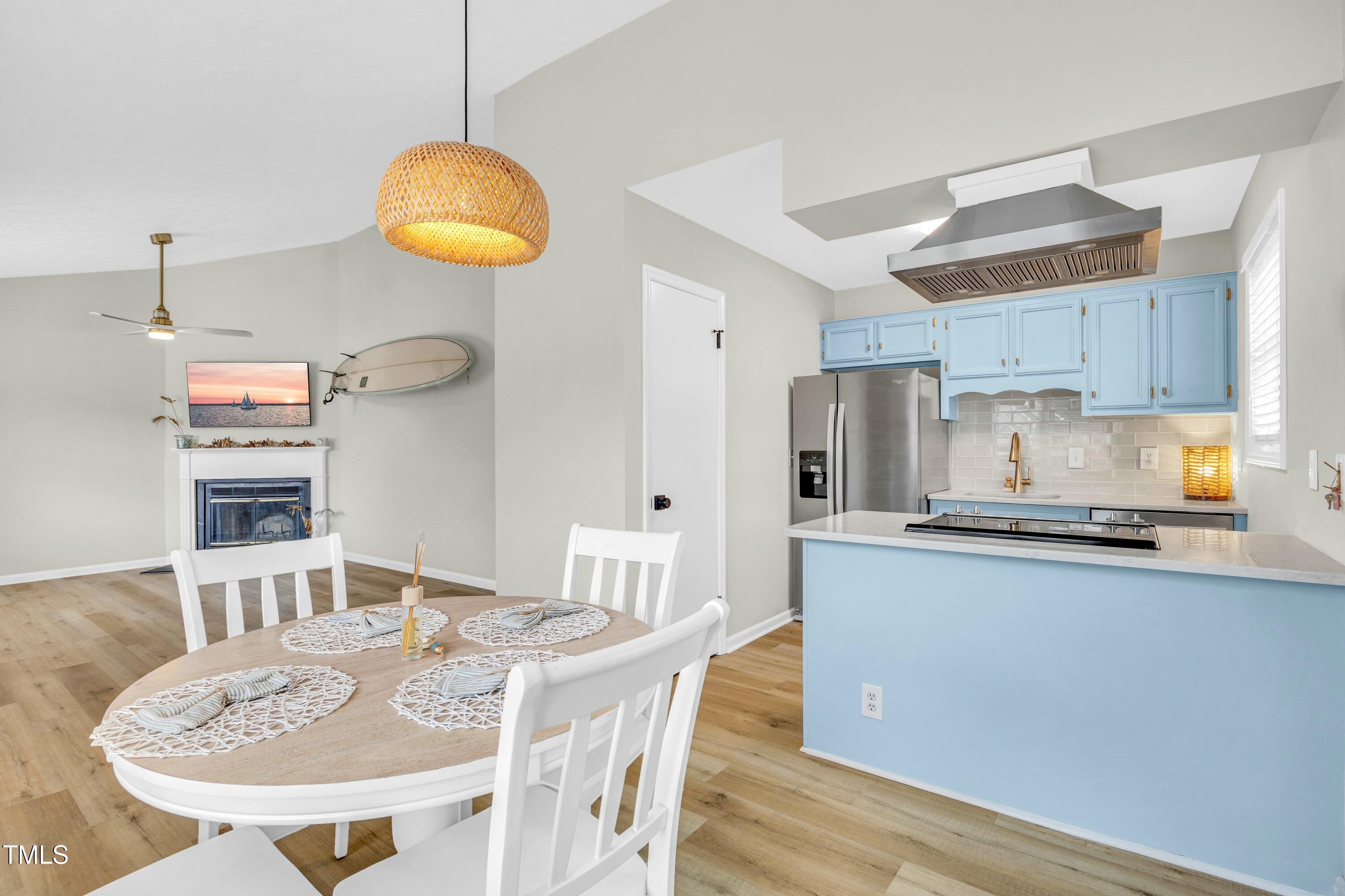 Open-plan kitchen and dining area with blue cabinets, stainless appliances, and an adjoining fireplace seating area.