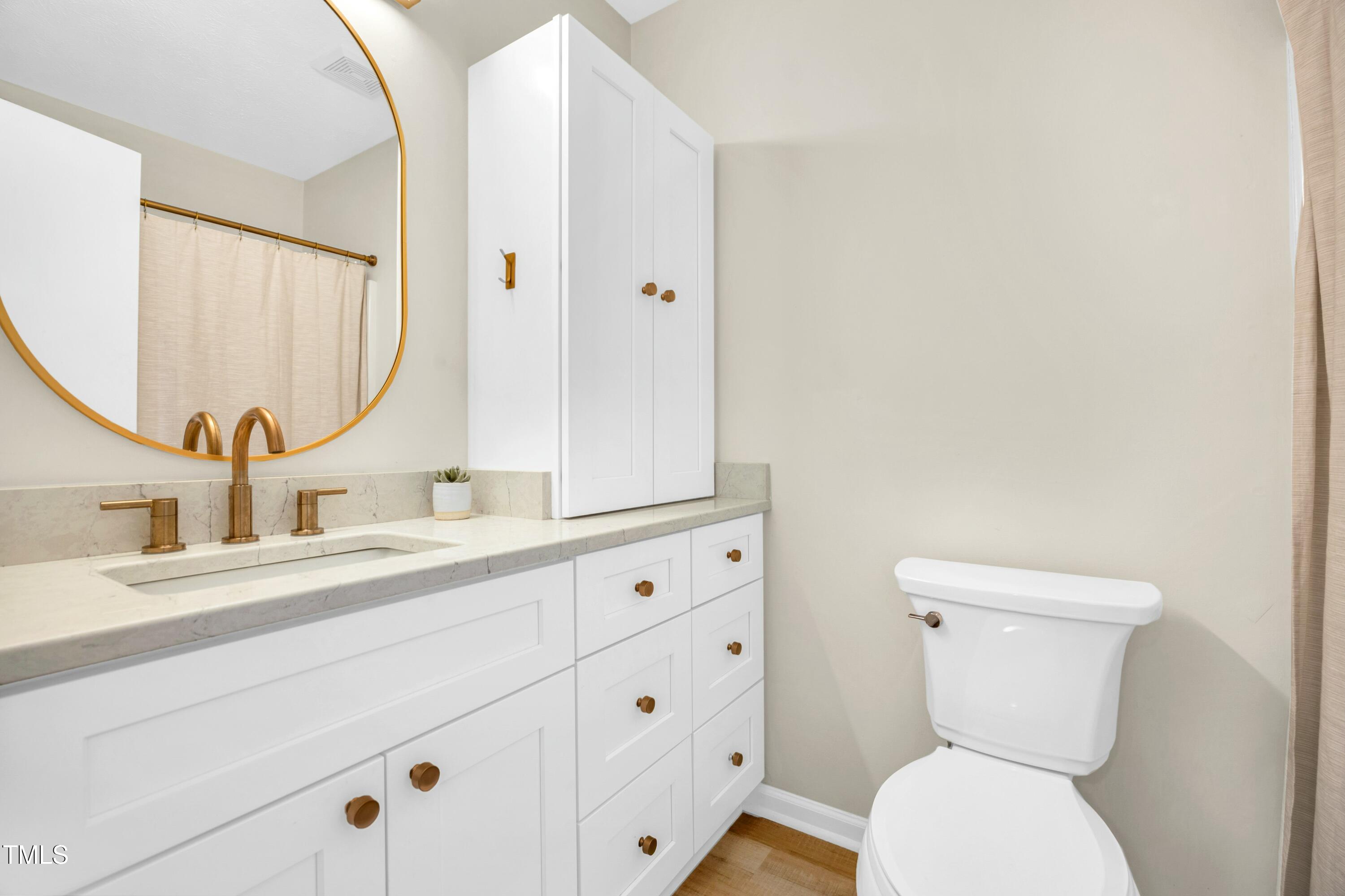 Bathroom with a white vanity, brass fixtures, round mirror, and toilet.