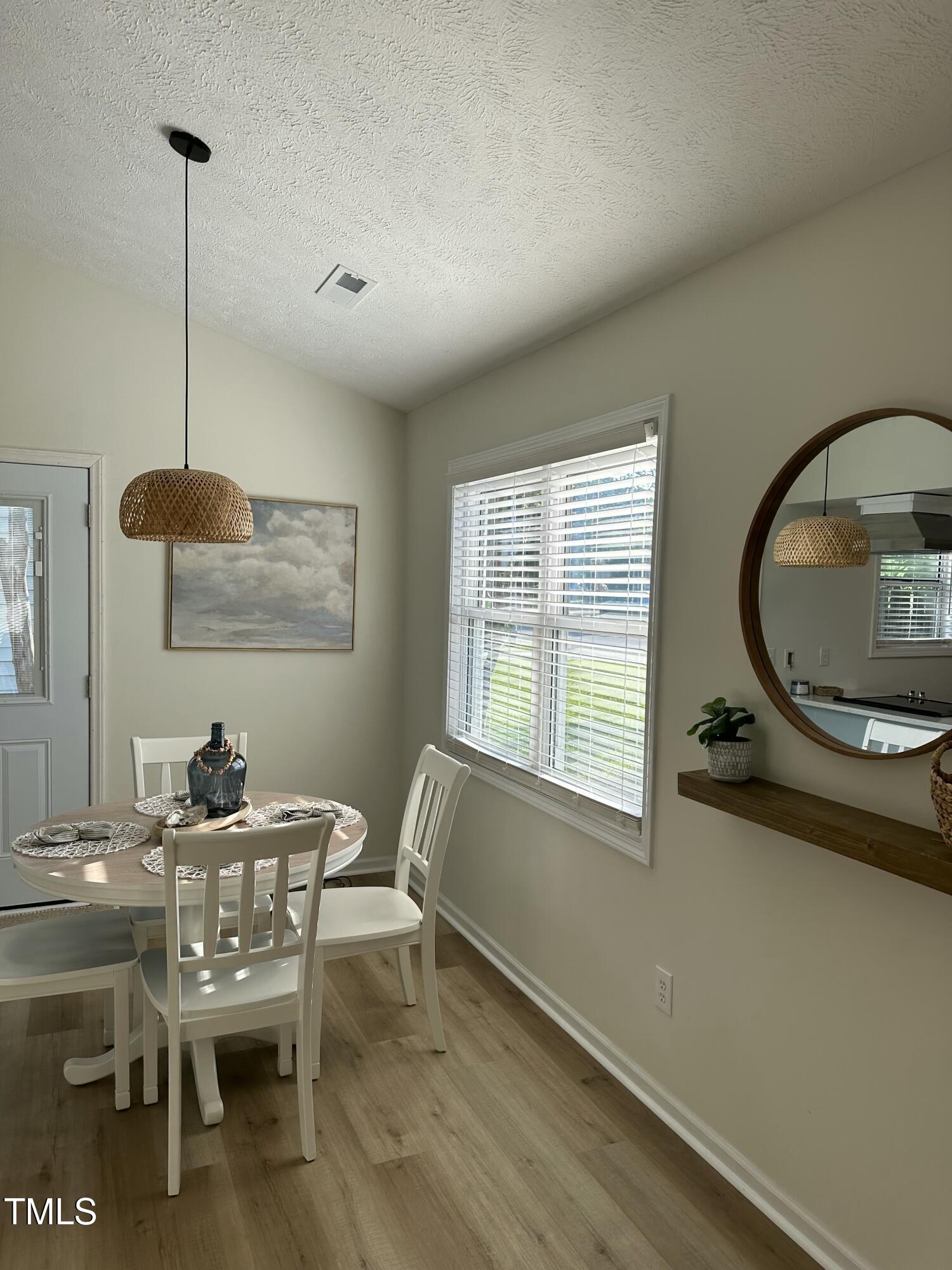 Dining area with a round table, white chairs, woven pendant light, and large window.