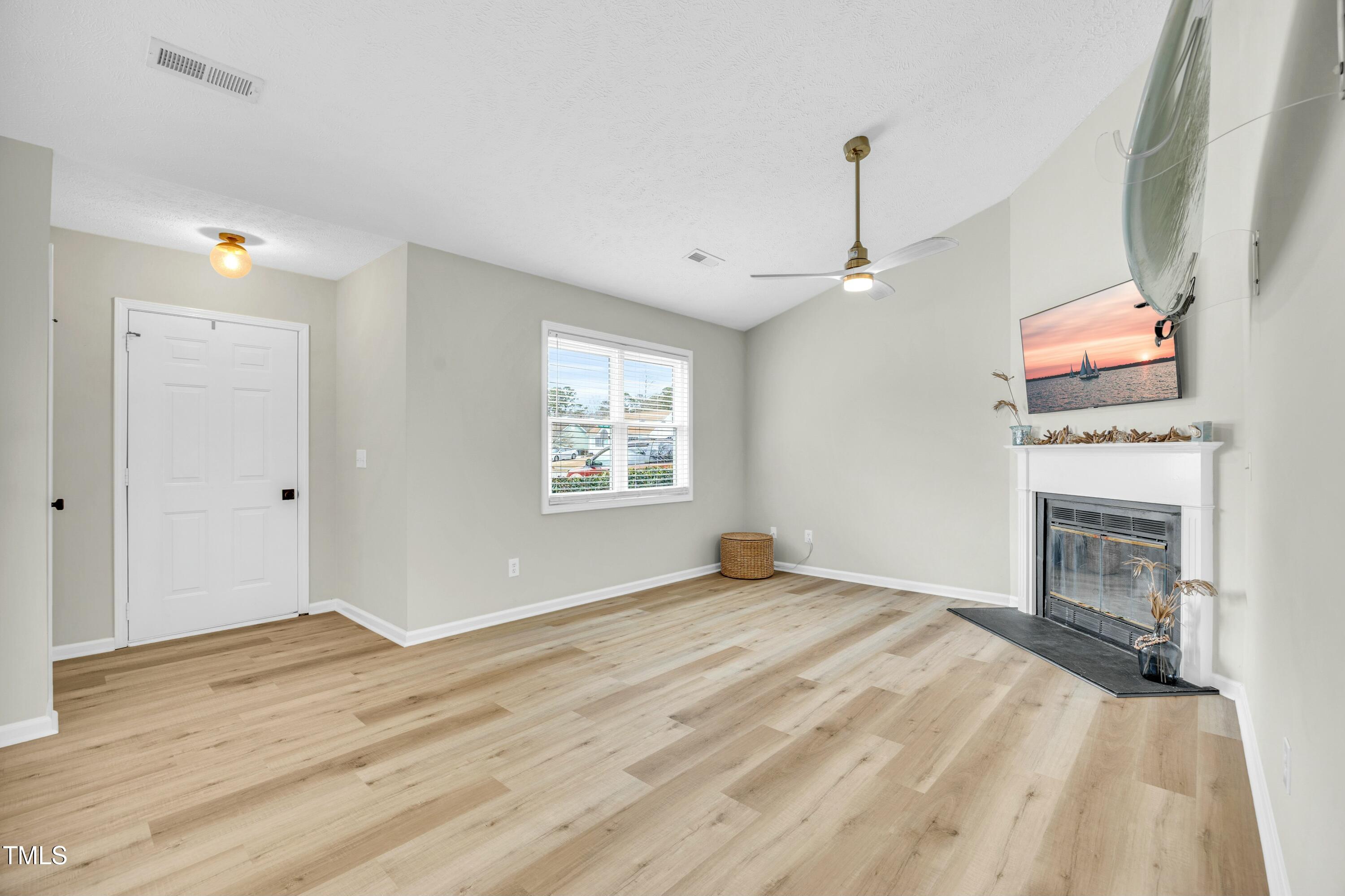 Living room with light wood floors, a white fireplace, ceiling fan, and wall-mounted surfboard.
