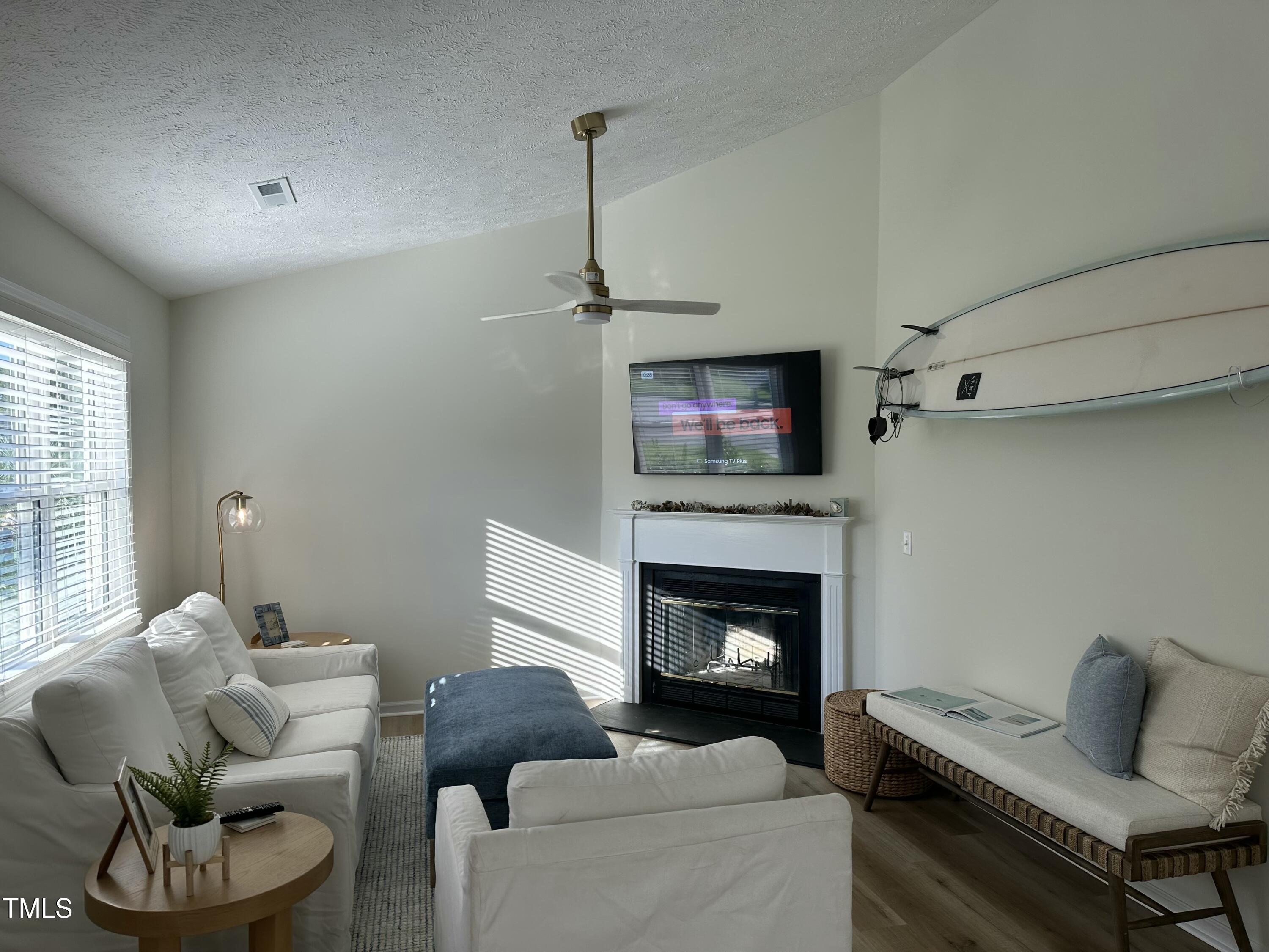 Living room with a fireplace, white sofas, blue ottoman, and a surfboard mounted on the wall.