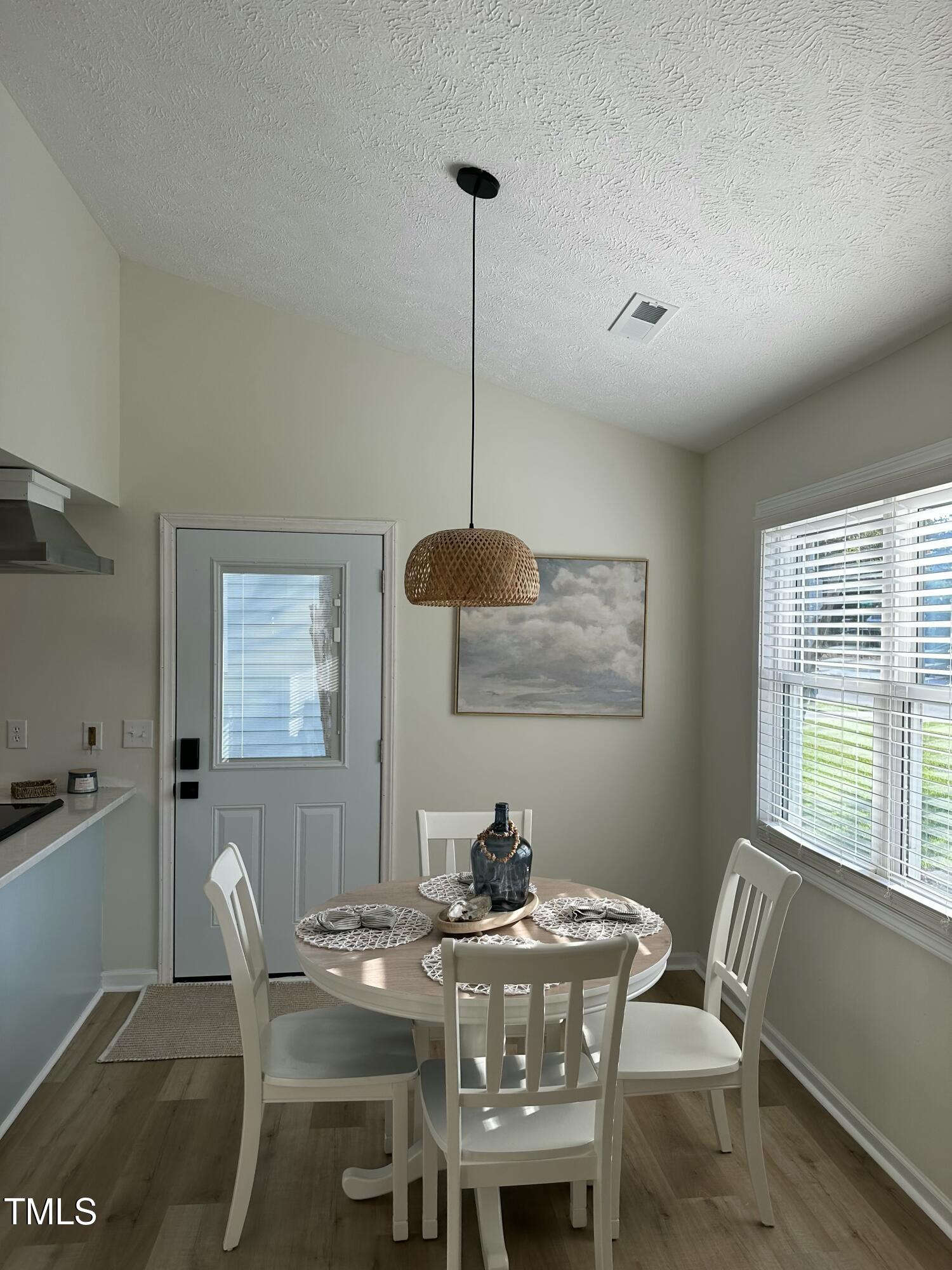 Dining area with a round table, white chairs, woven pendant light, and a glass-paneled door.