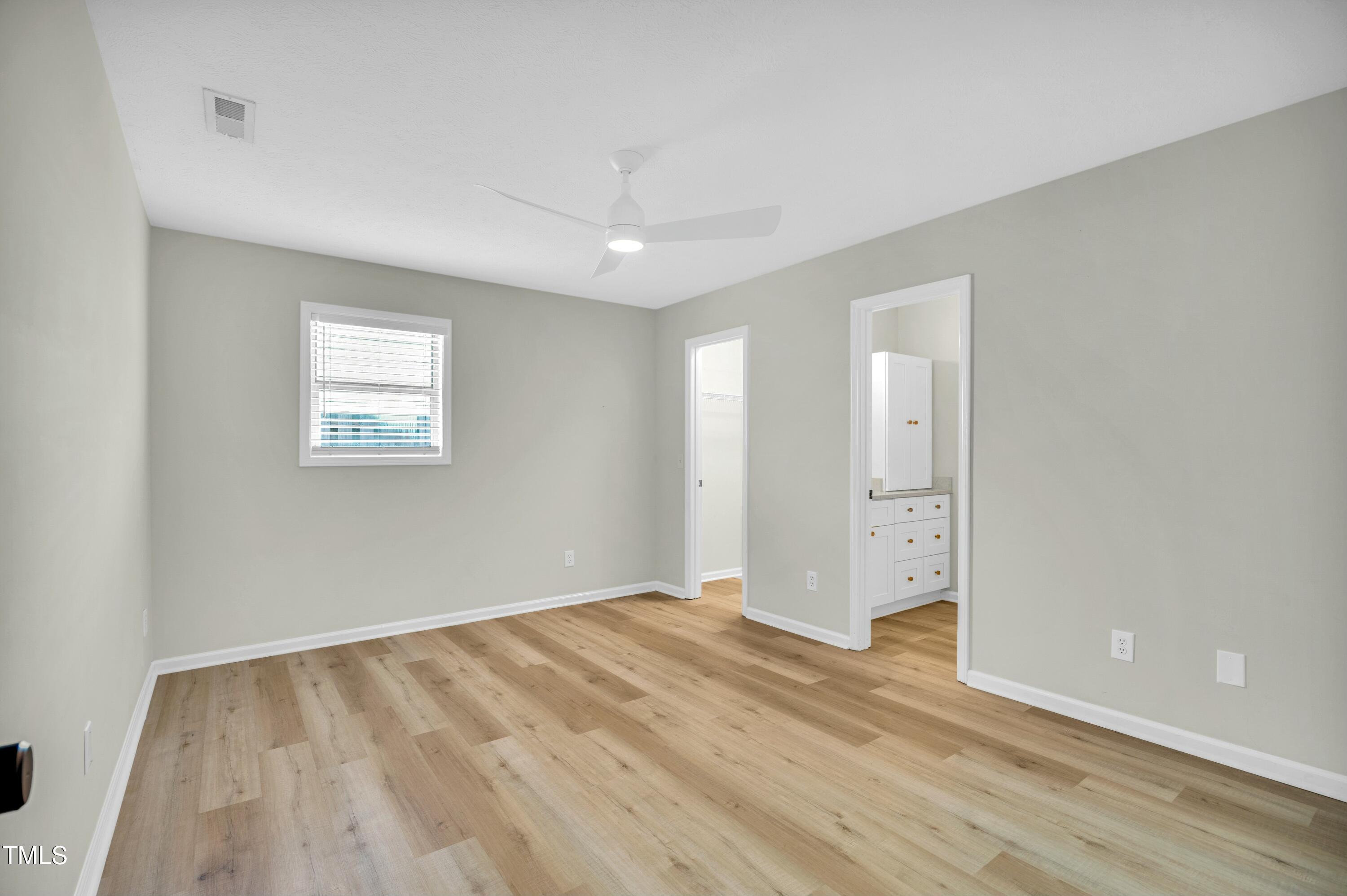 Empty bedroom with wood-look flooring, a ceiling fan, and a doorway to a built-in vanity.