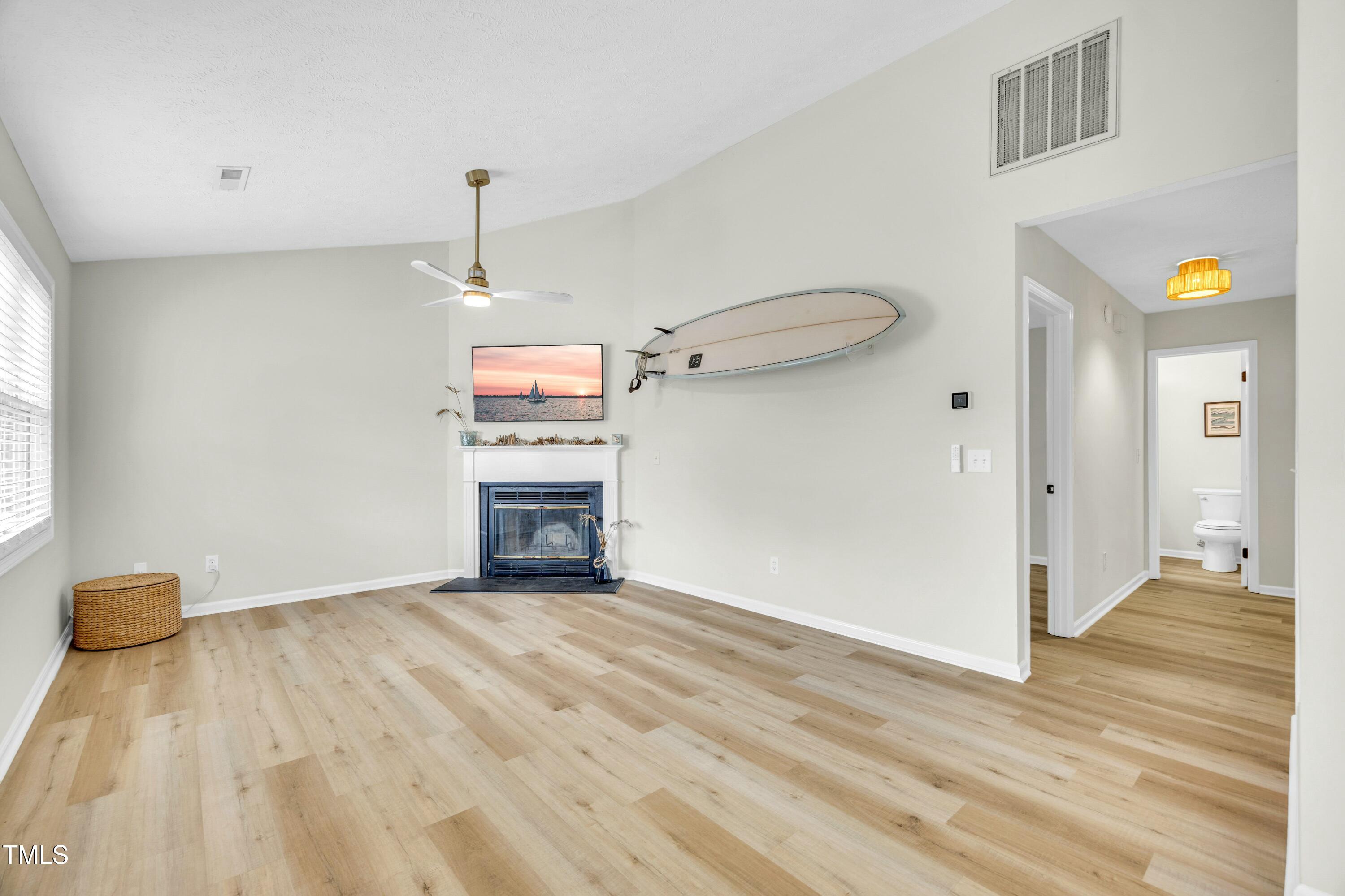 Living room with a fireplace, mounted surfboard, and light wood-look flooring.