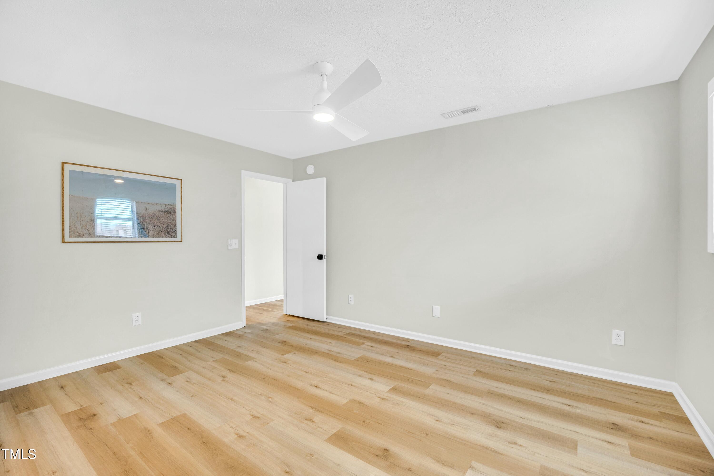 Vacant bedroom with light wood-look flooring and a white ceiling fan.