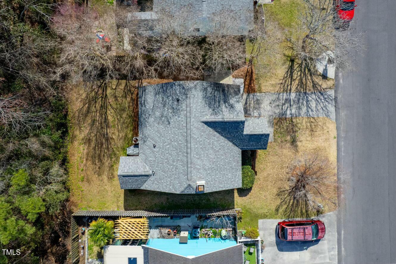 Aerial view of a house with a backyard pool and pergola beside a wooded lawn.