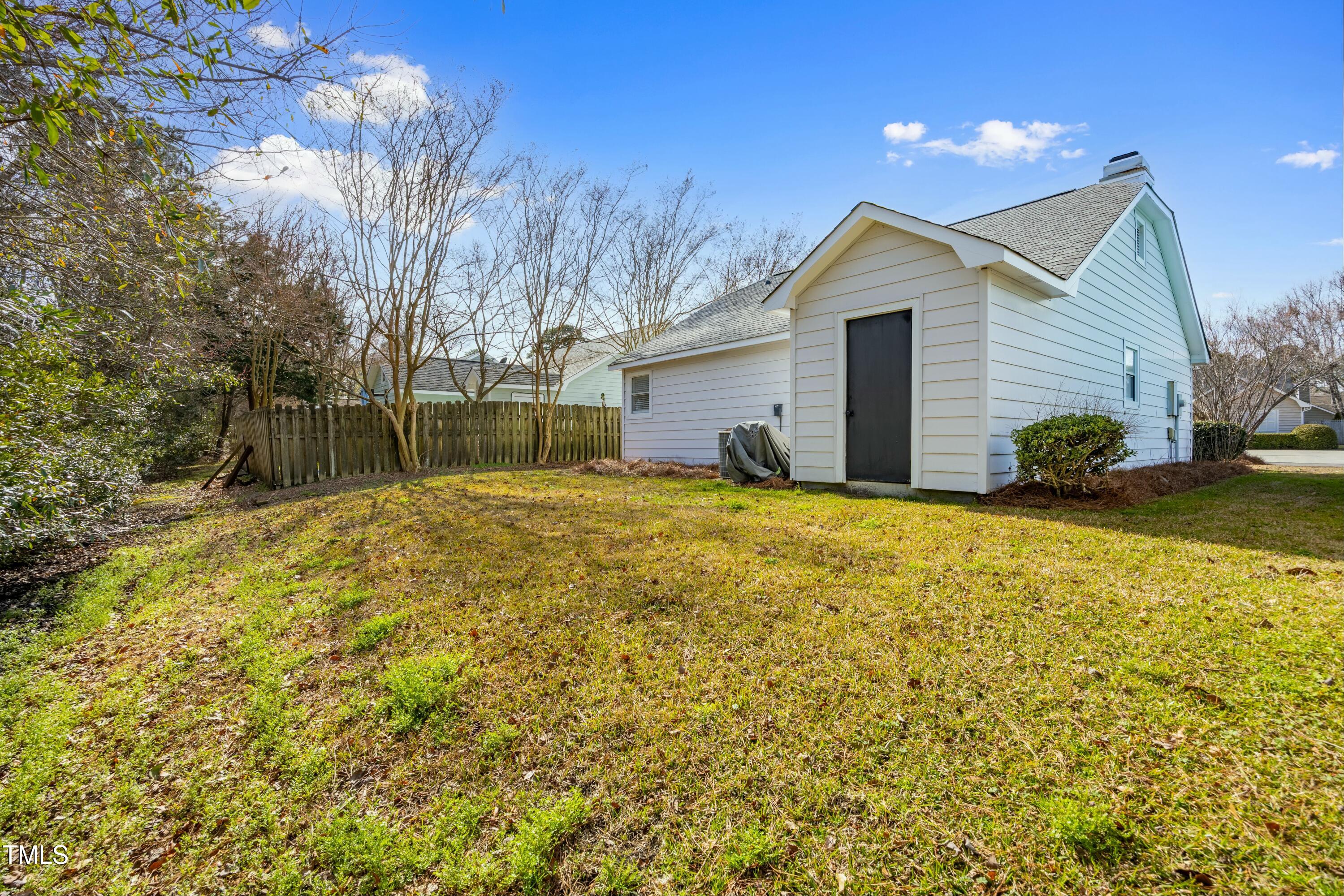 White house side and rear with a dark outbuilding door, grassy yard, and wooden fence.