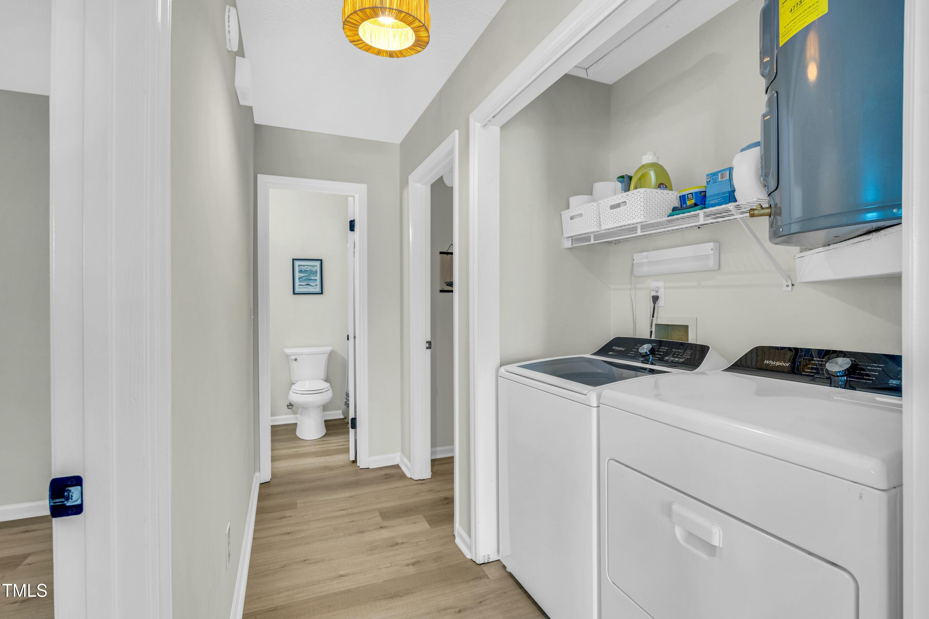 Laundry room with white washer and dryer, storage shelf, and doorway to a bathroom.