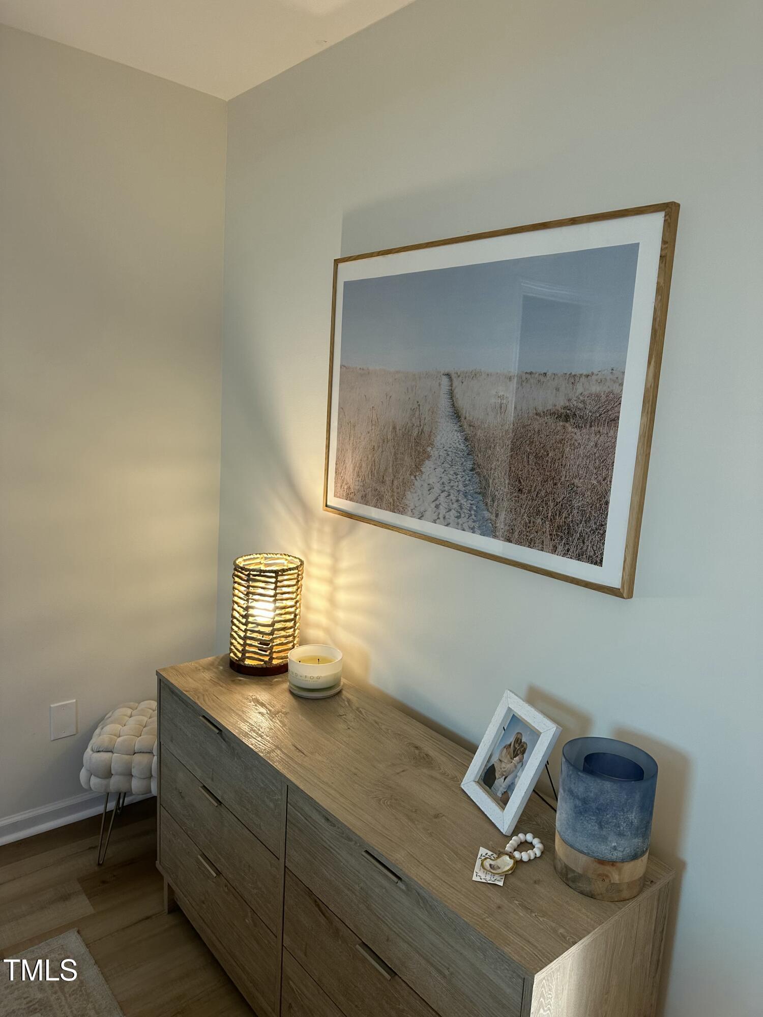 Wood dresser with a glowing woven lamp and framed landscape photograph above it.
