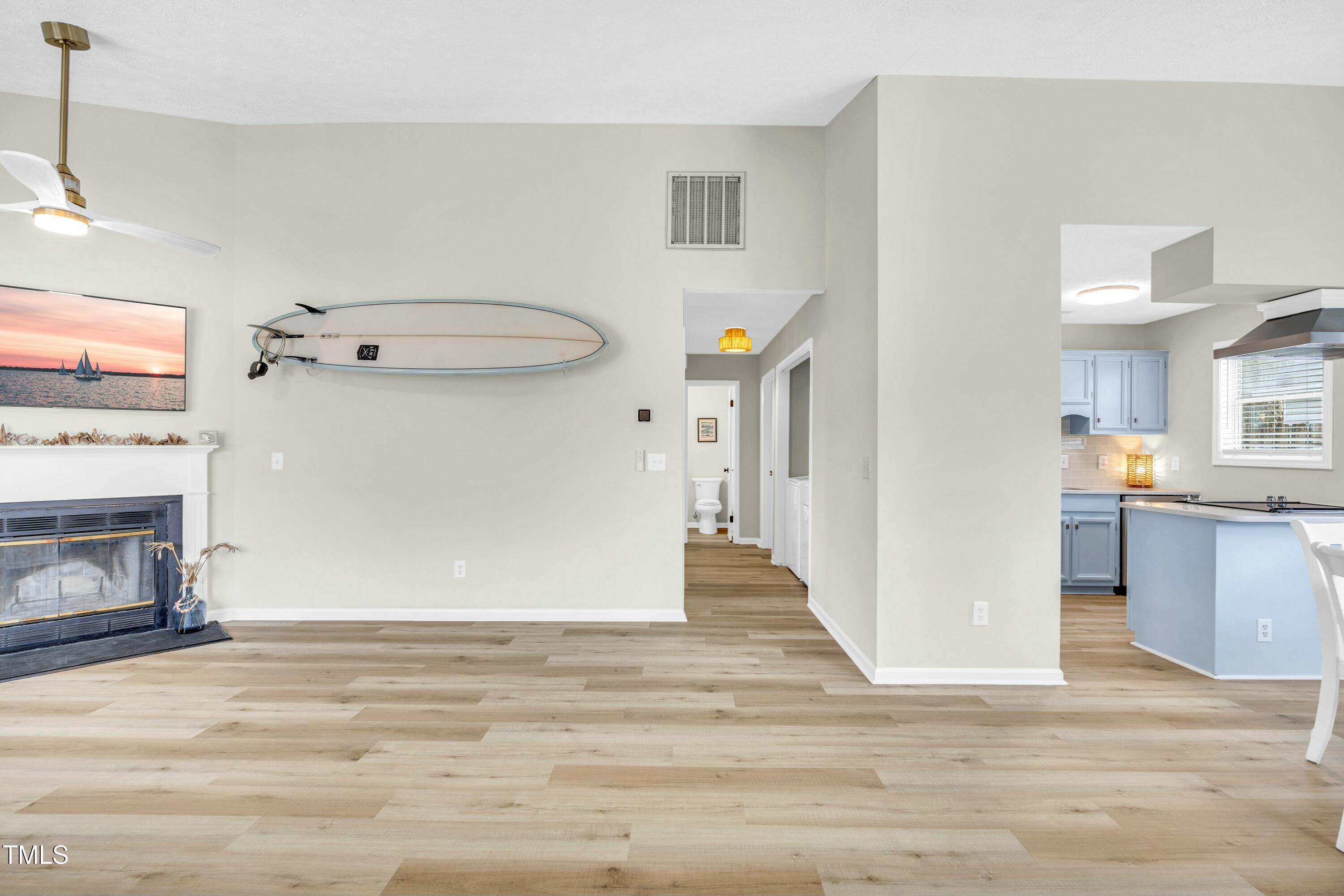 Open-plan living room and kitchen with a fireplace, wall-mounted surfboard, and light blue kitchen cabinets.
