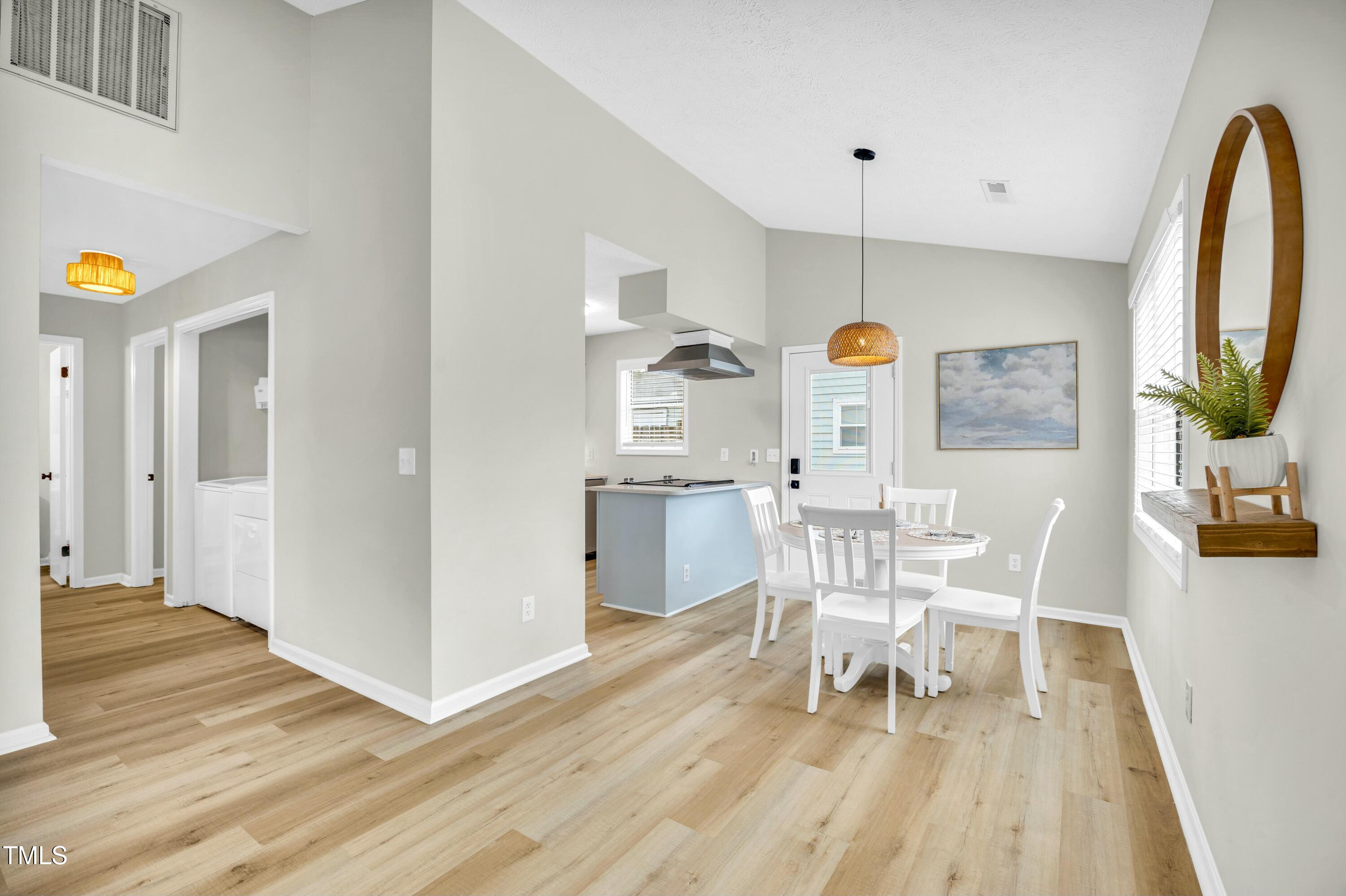 Open dining area with white table and chairs beside a pale blue kitchen island and light wood floors.