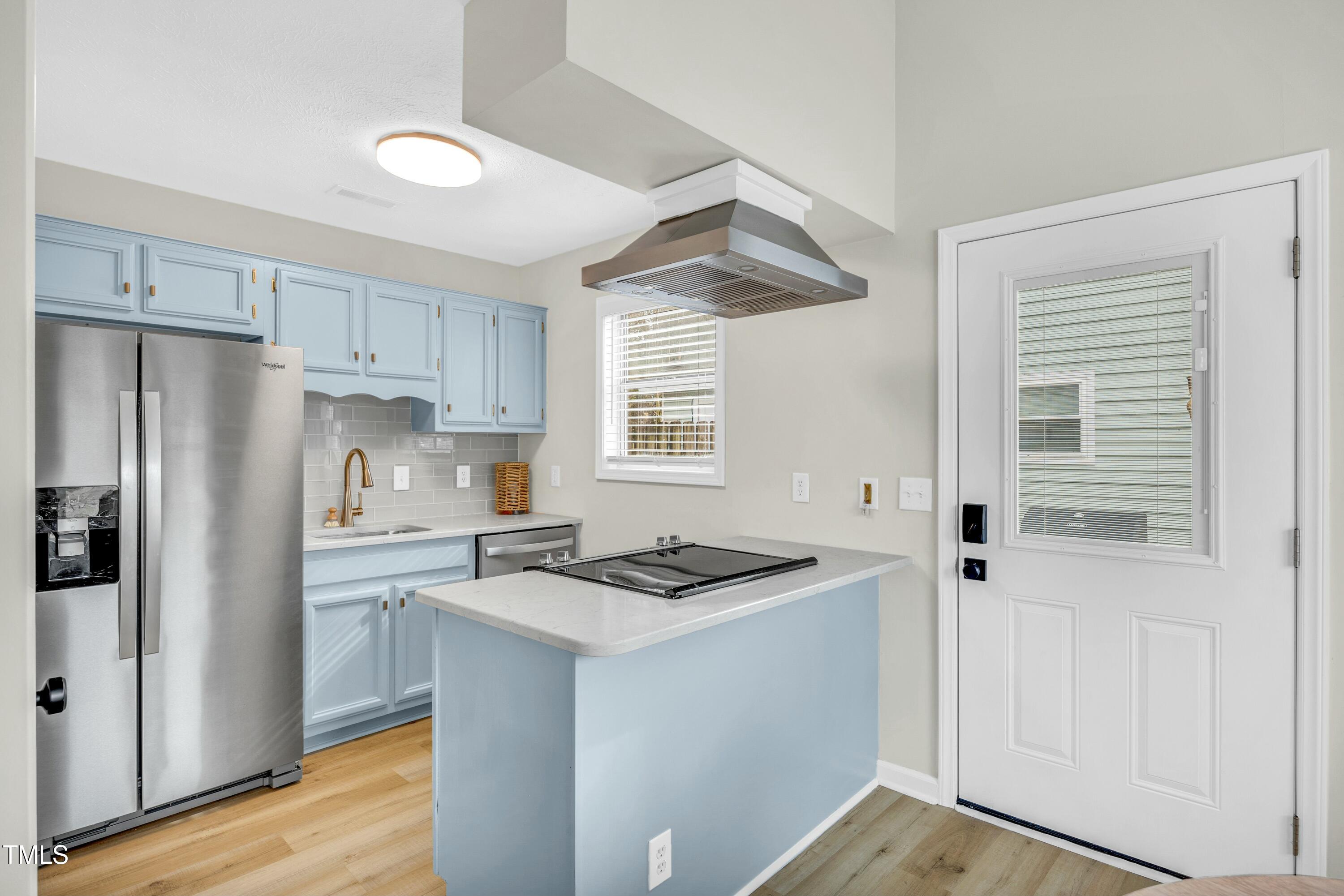 Kitchen with pale blue cabinets and island, stainless steel appliances, and a white door with blinds.