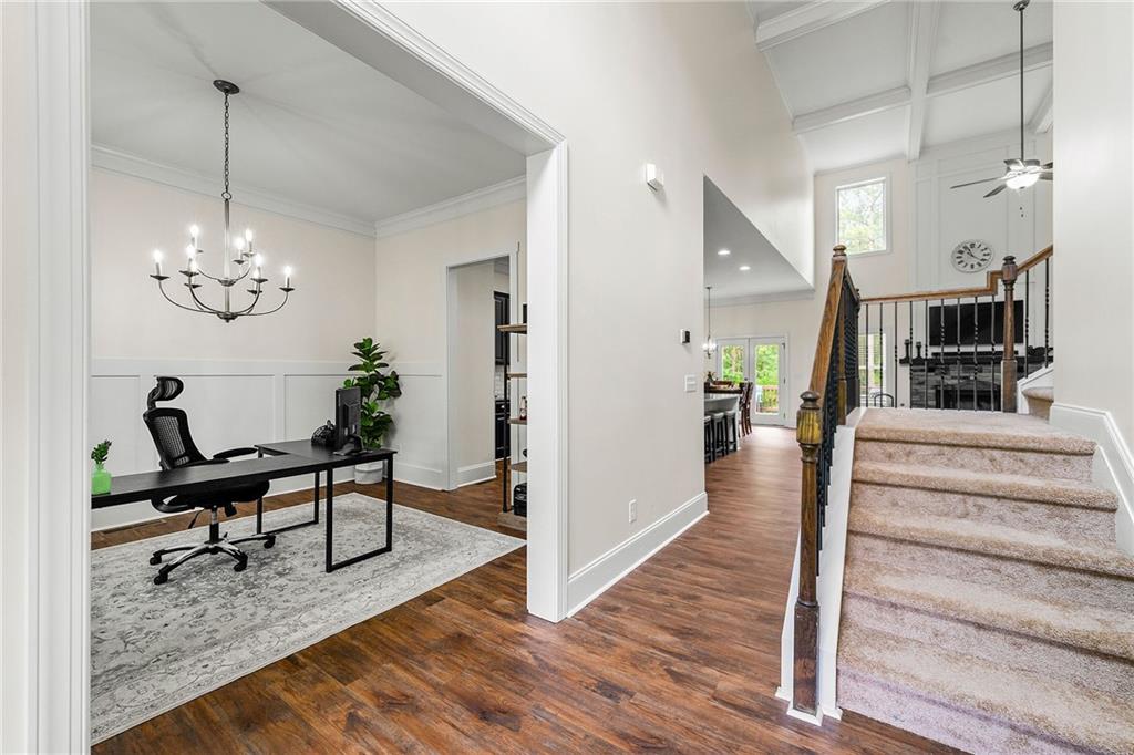 Foyer with carpeted staircase and adjoining home office with a desk and chandelier.