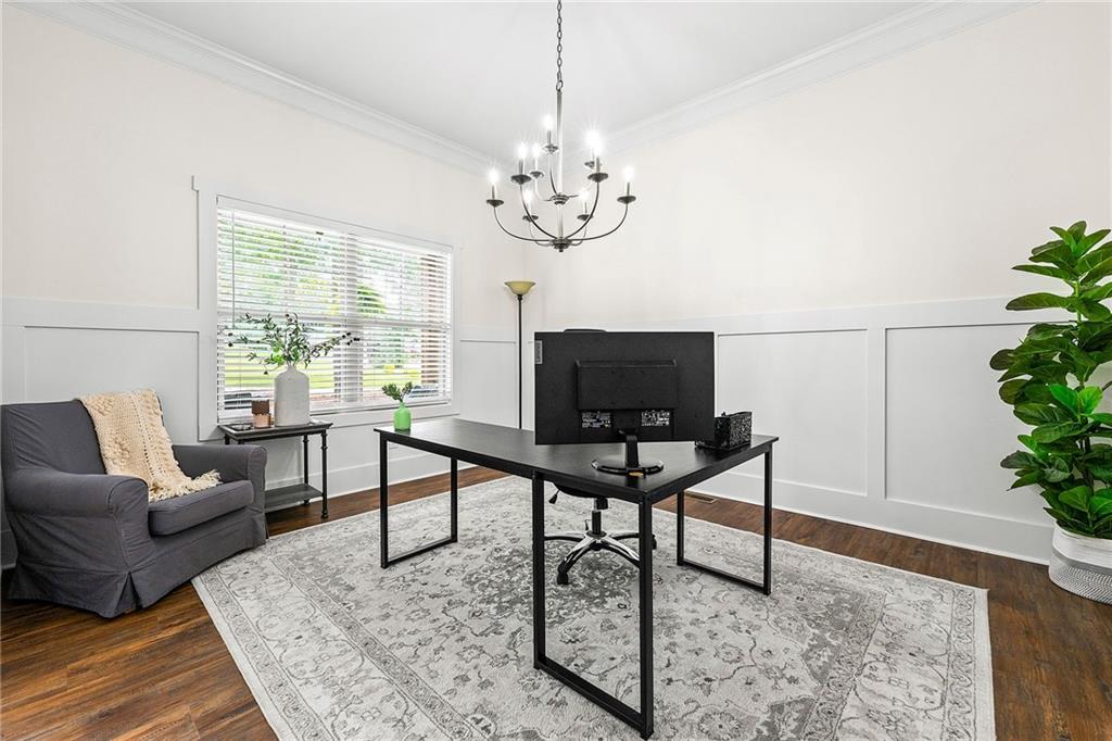 Bright home office with a black desk, gray armchair, large window, and chandelier.