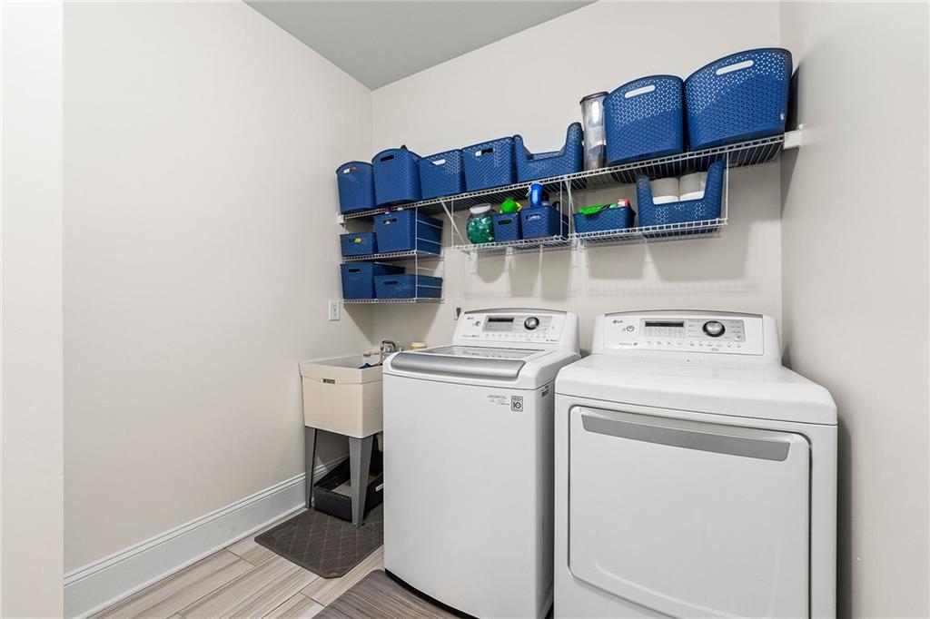 Laundry room with a washer, dryer, utility sink, and wall shelves holding blue storage bins.