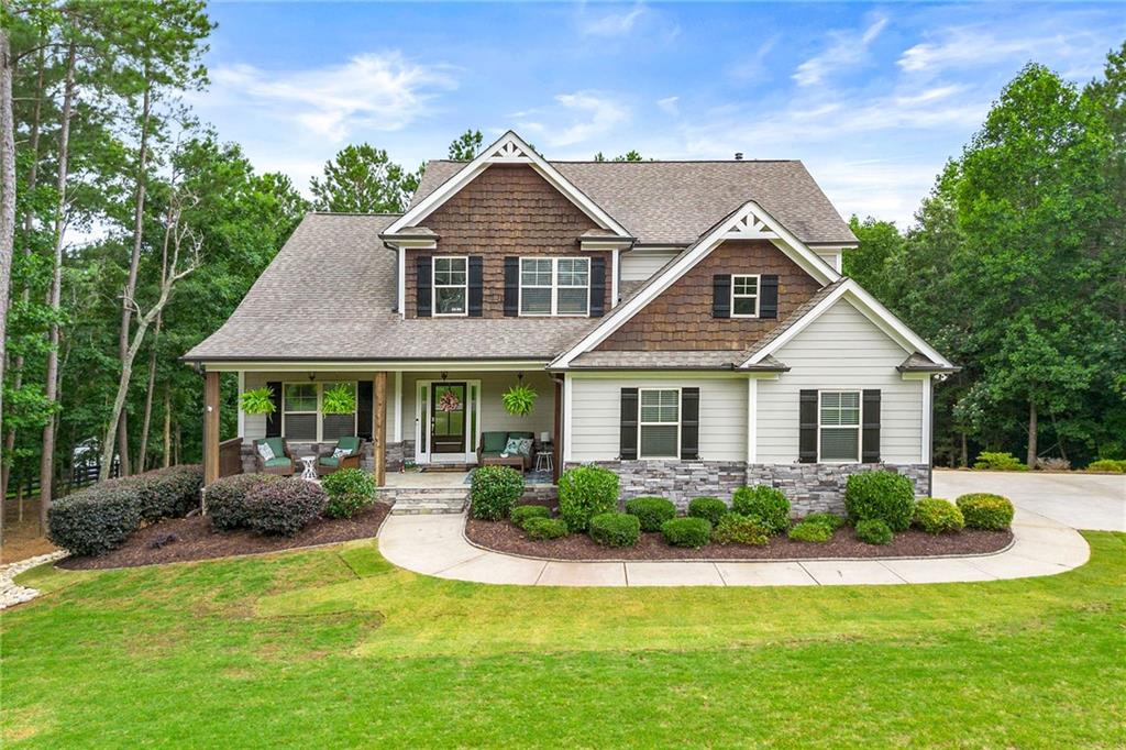 Two-story house with brown shingle accents, stone veneer, and a covered porch amid mature trees.