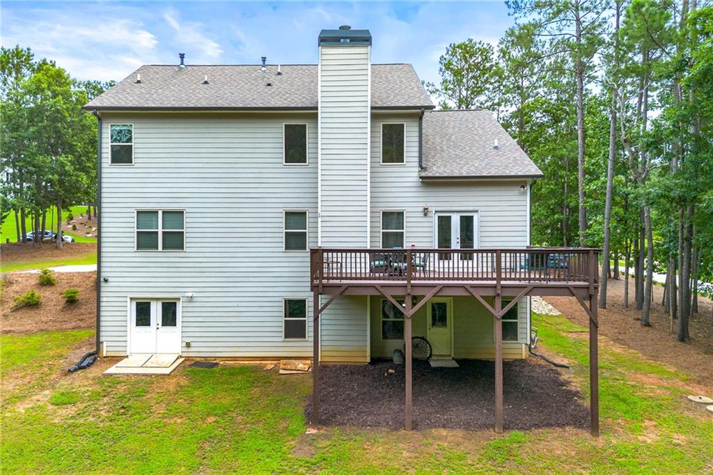 Rear of a two-story house with a raised wooden deck overlooking a tree-lined yard.