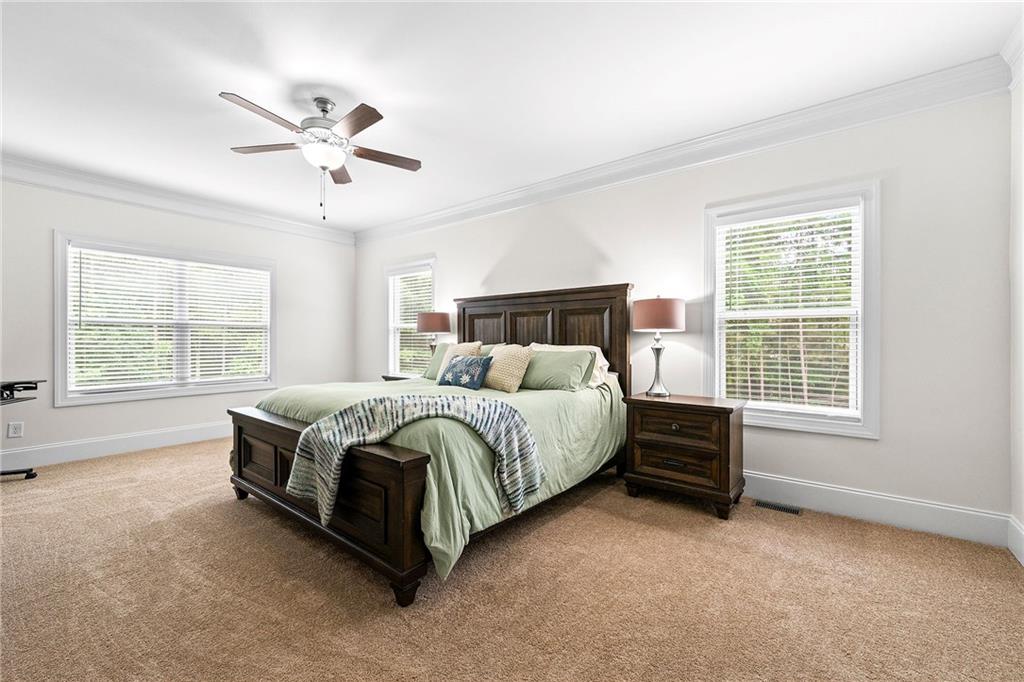 Furnished bedroom with a dark wood bed, pale green bedding, beige carpet, and three bright windows.