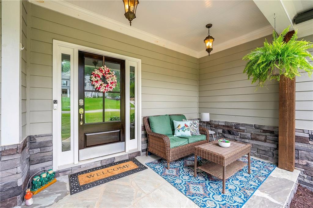 Covered front porch with a dark entry door, wicker seating, and a blue patterned rug.