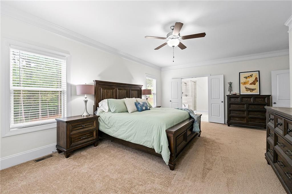 Furnished bedroom with a dark wood bed, pale green bedding, beige carpet, and ceiling fan.