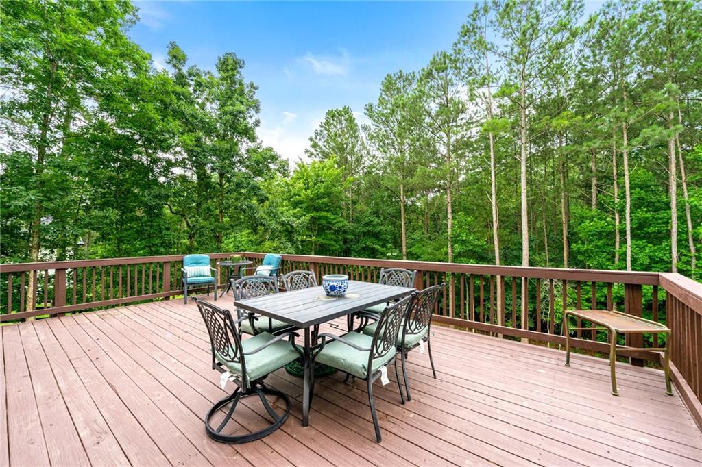 Wooden deck with outdoor dining furniture overlooking tall trees.