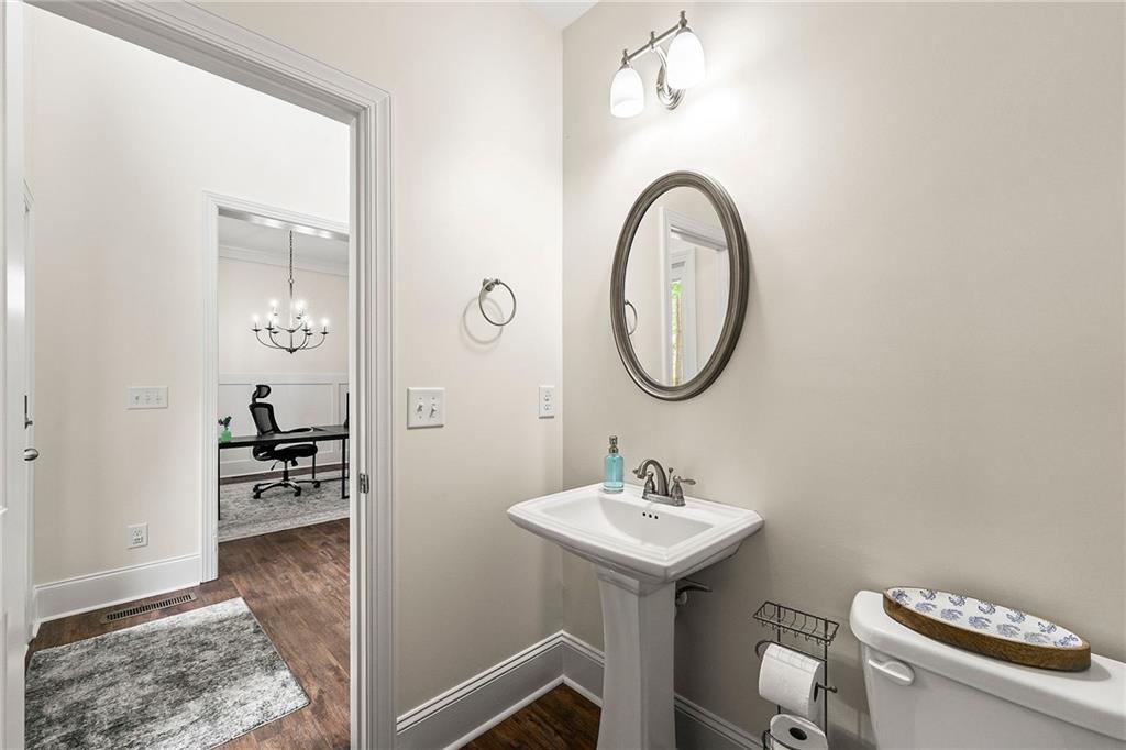 Powder room with a pedestal sink, oval mirror, and doorway to a furnished office.