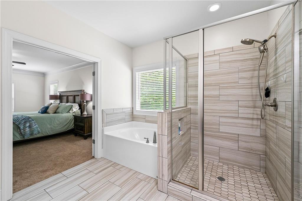 Bathroom with a tiled glass-enclosed shower and bathtub beside a window, with an adjoining bedroom visible.