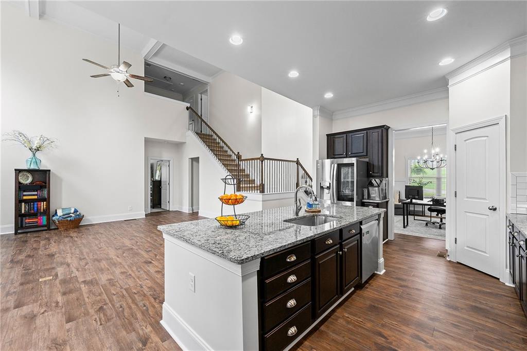 Open kitchen with a granite island, dark cabinetry, and a staircase in a high-ceilinged living area.