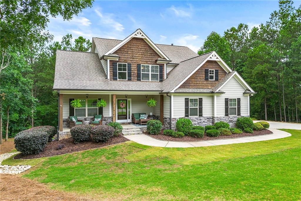 Two-story white-sided home with stone accents, a covered porch, and landscaped lawn.