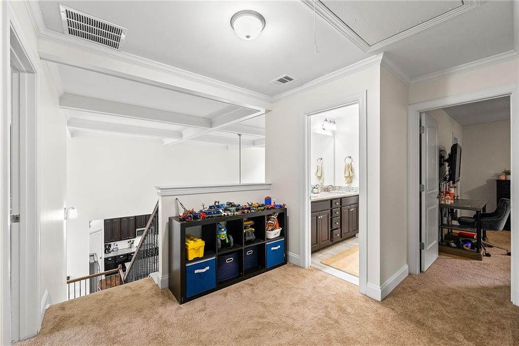 Carpeted upstairs landing with toy storage, a stair railing, and doorways to a bathroom and office.