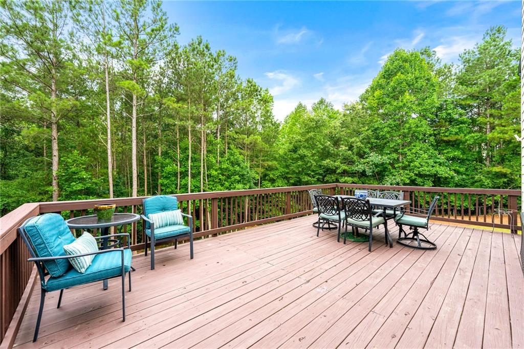 Furnished wooden deck with turquoise chairs and dining set overlooking dense green woods.