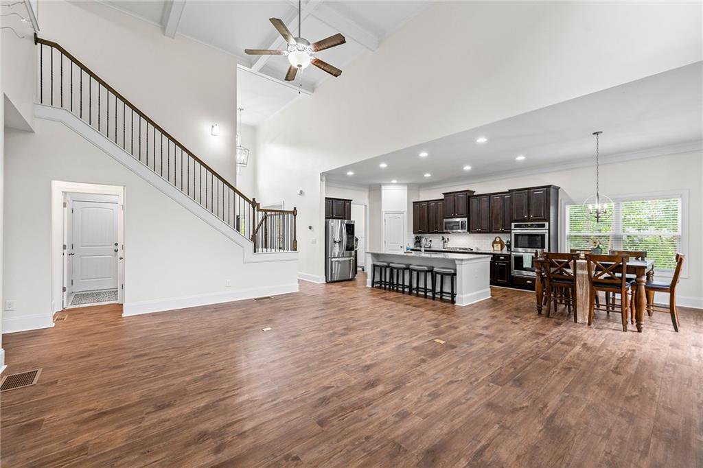 Open-plan kitchen and dining area with a large island, dark cabinets, hardwood floors, and staircase.