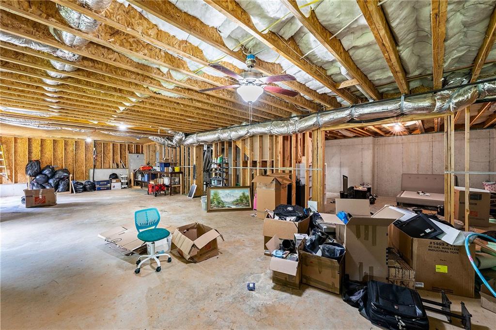 Unfinished basement with exposed ceiling joists, ductwork, and scattered storage boxes.