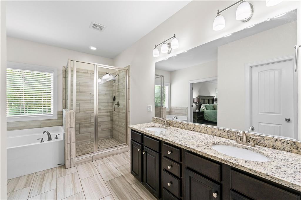 Primary bathroom with double vanity, granite counter, glass shower, and soaking tub beside a window.