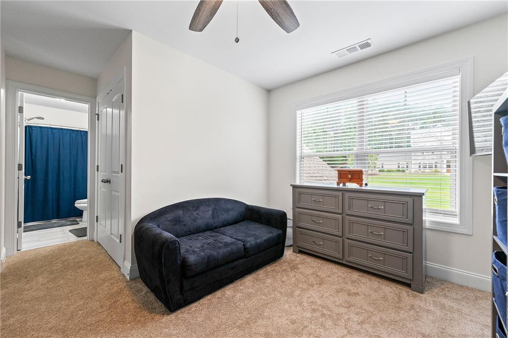 Carpeted bedroom with a dark sofa, gray dresser, and window overlooking a green lawn.